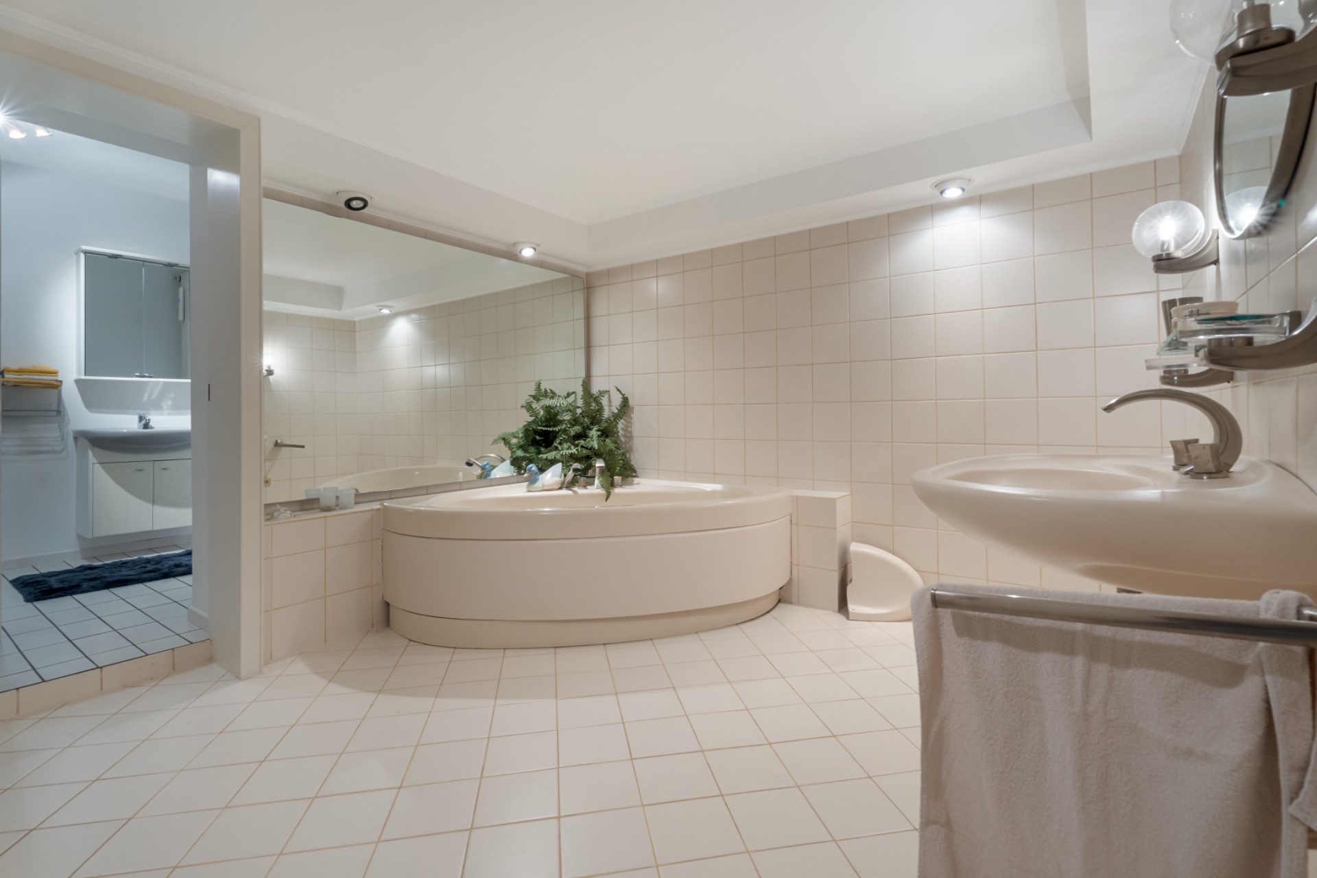 Helles Badezimmer mit Eckbadewanne, großem Spiegel, Waschbecken und Handtuch.