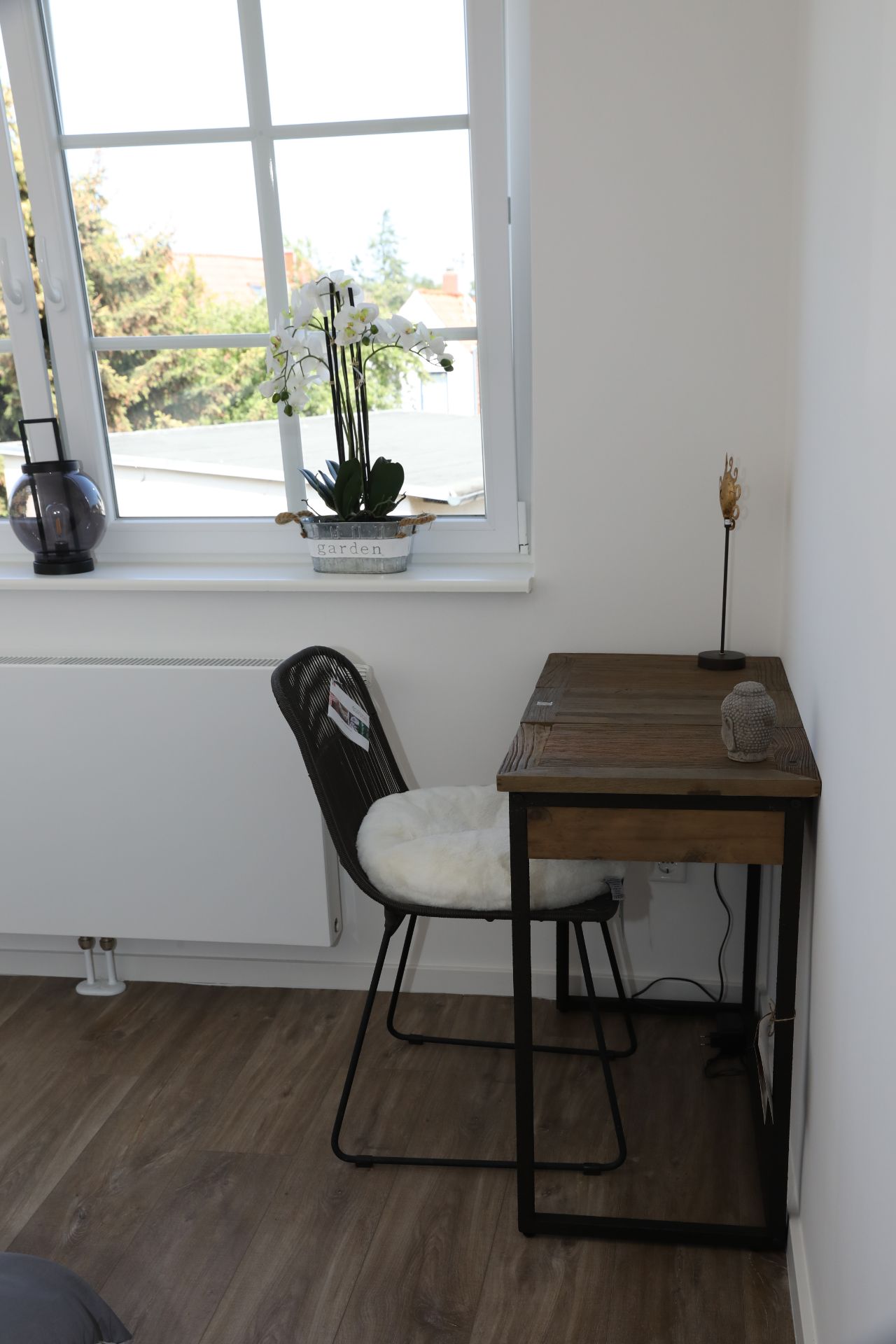 Kleiner Schreibtisch mit Stuhl an einem Fenster, Pflanze und Dekoration darauf.