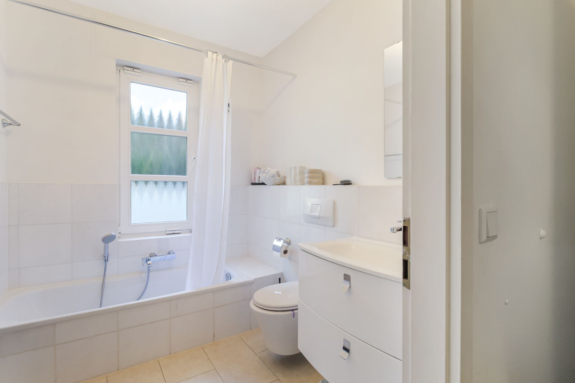Helles Badezimmer mit Badewanne, Duschvorhang, WC und Waschbecken, Fenster an der Wand.