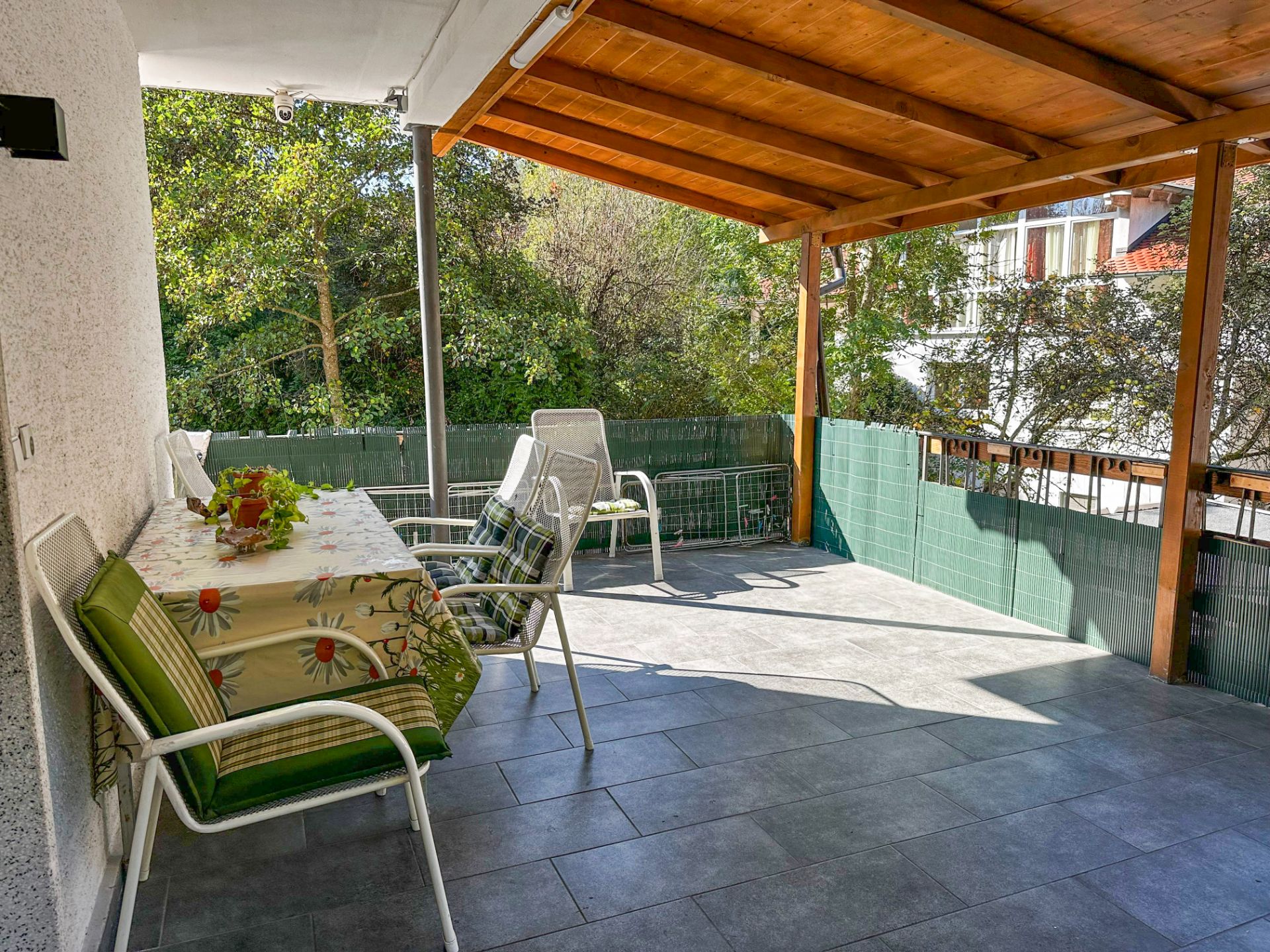 Überdachte Terrasse mit Tisch, Stühlen und Blick auf Bäume.