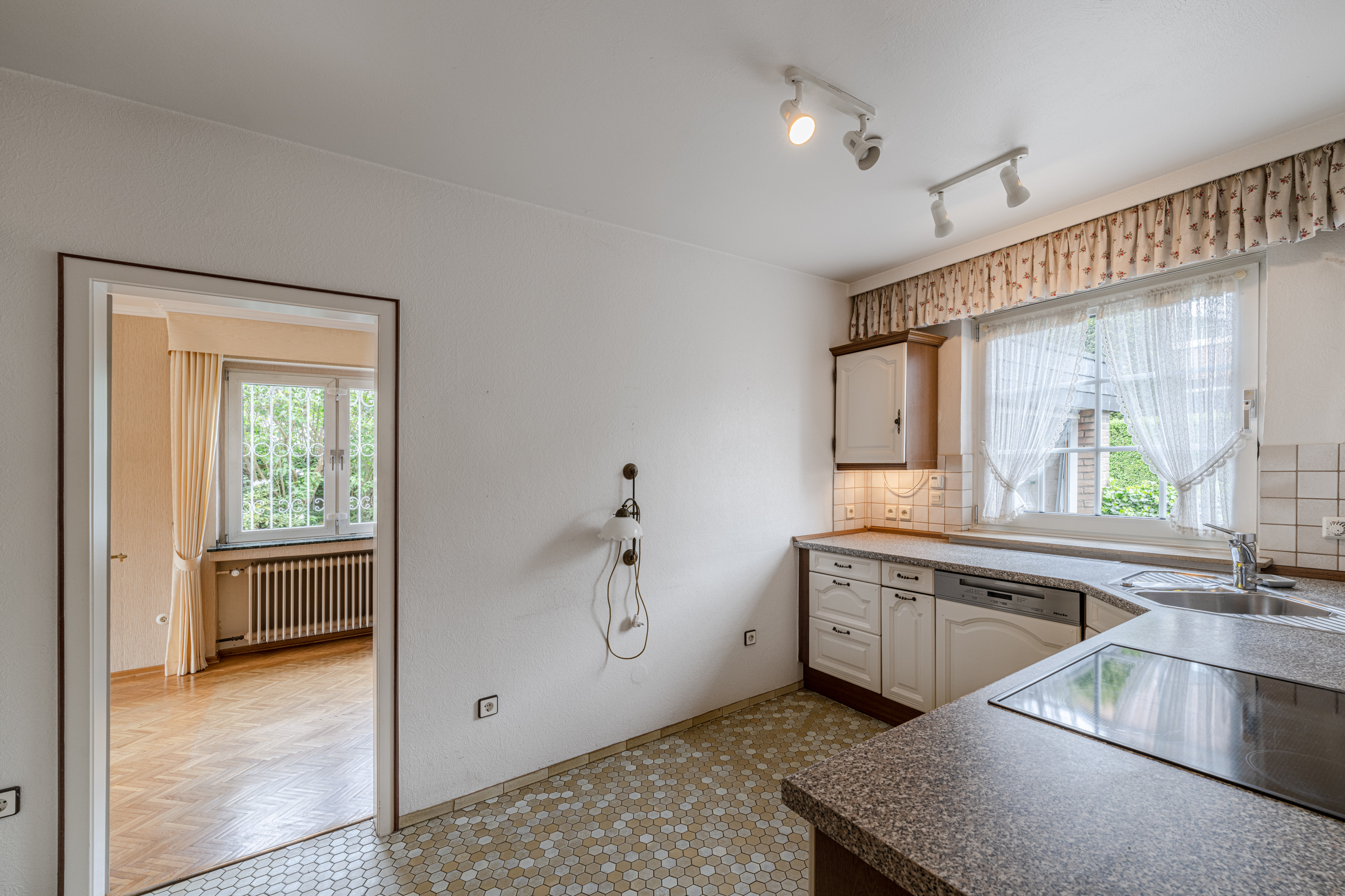 Helle Küche mit Eckspüle, weißen Schränken und Blick ins angrenzende Wohnzimmer.