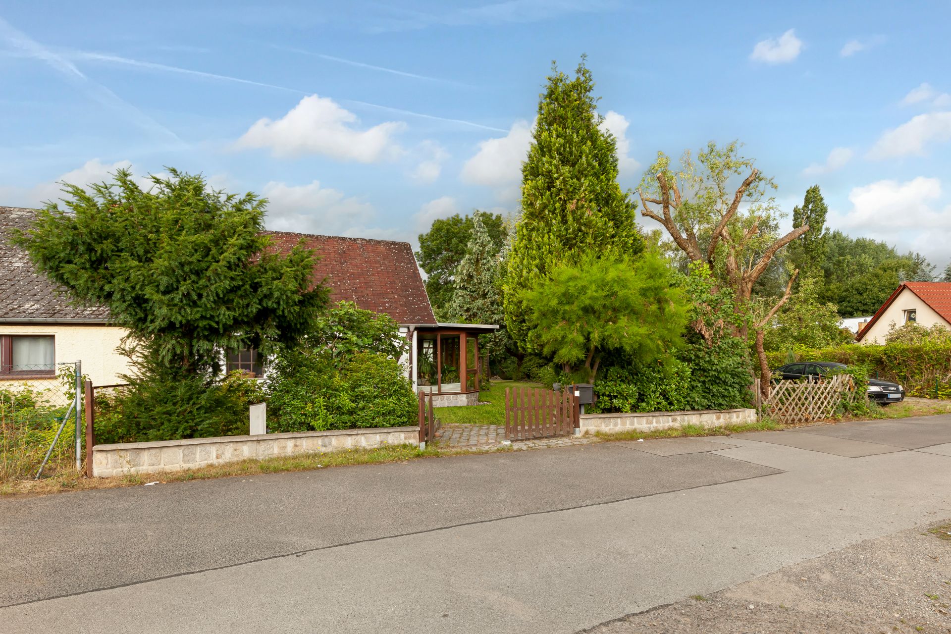Einfamilienhaus mit Vorgarten, Hecke und Zaun an einer ruhigen Straße.