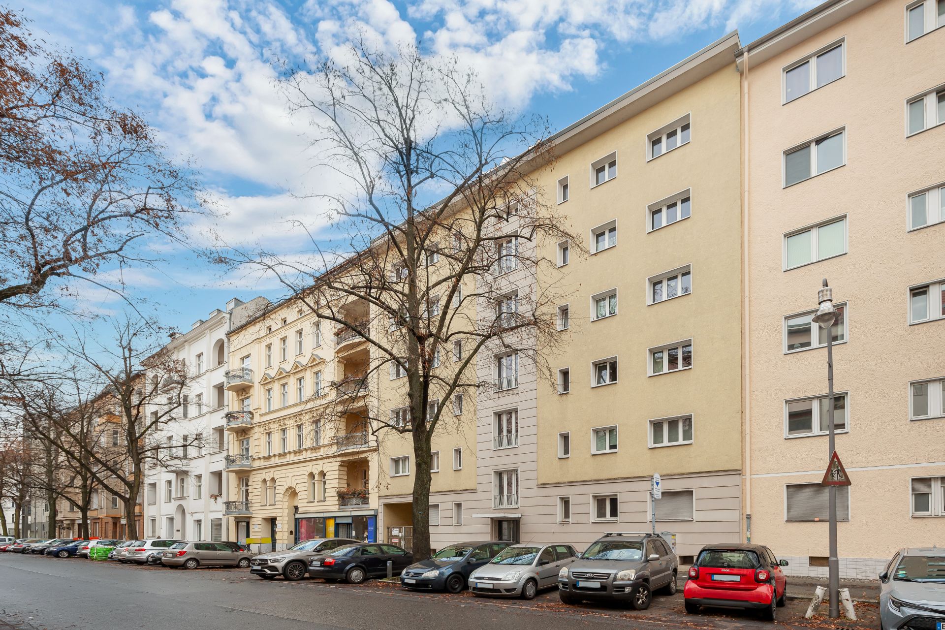 Mehrstöckige Wohnhäuser mit geparkten Autos und kahlen Bäumen an einer ruhigen Straße.