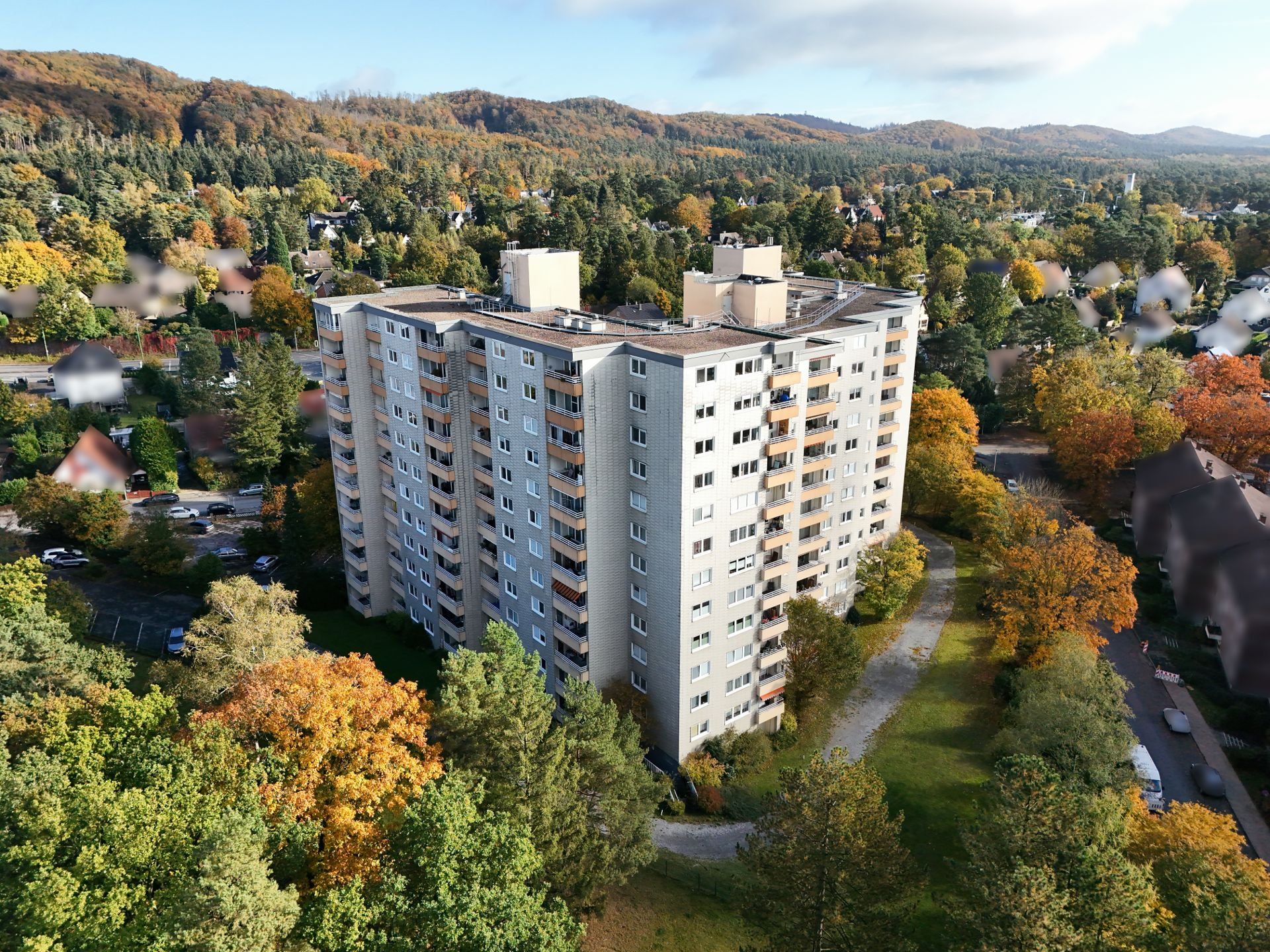 Mehrstöckiges Wohnhaus umgeben von Bäumen und Grünflächen in herbstlicher Umgebung.