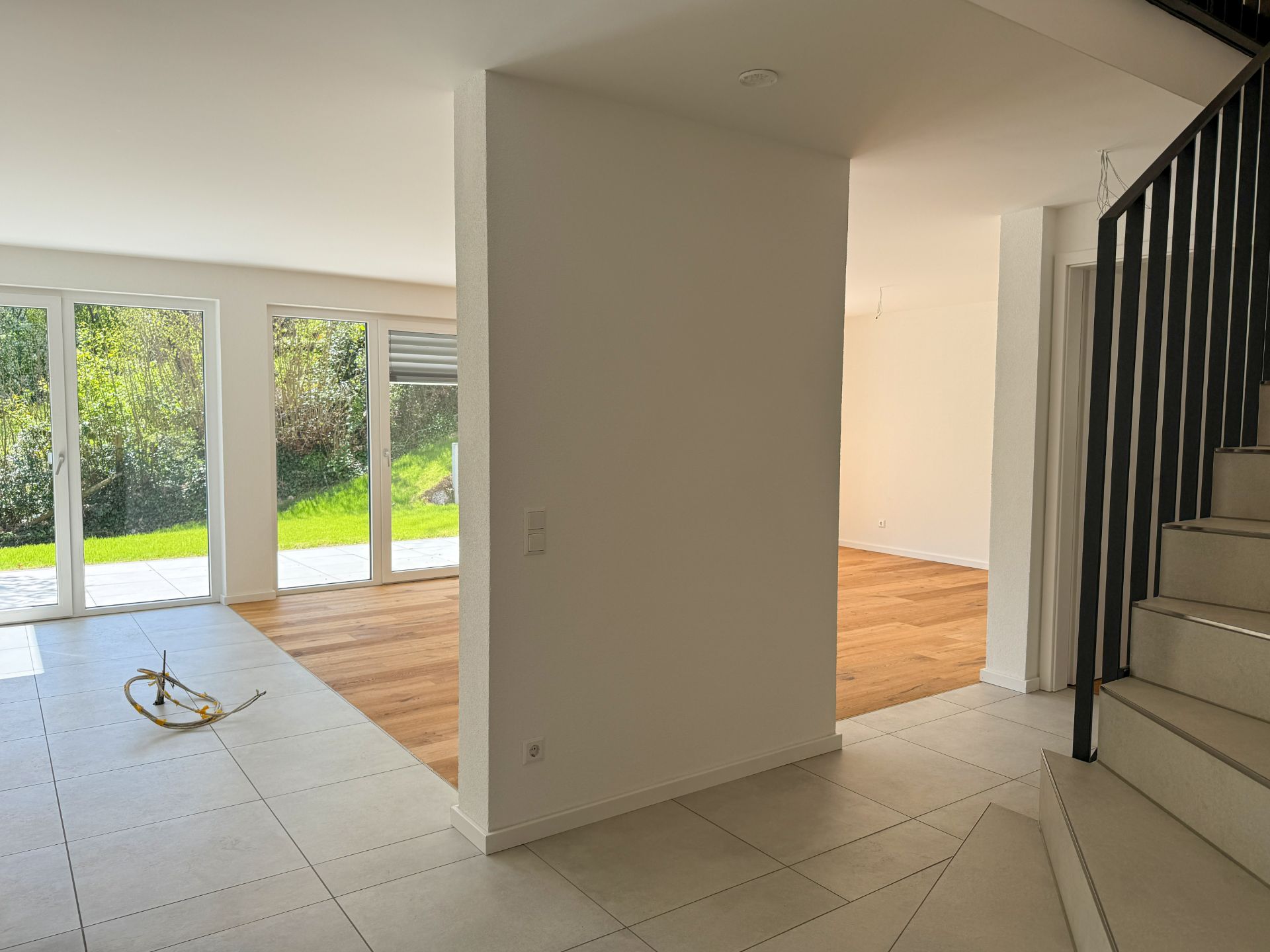 Heller Eingangsbereich mit Treppe, Fliesenboden und großem Fenster zum Garten.