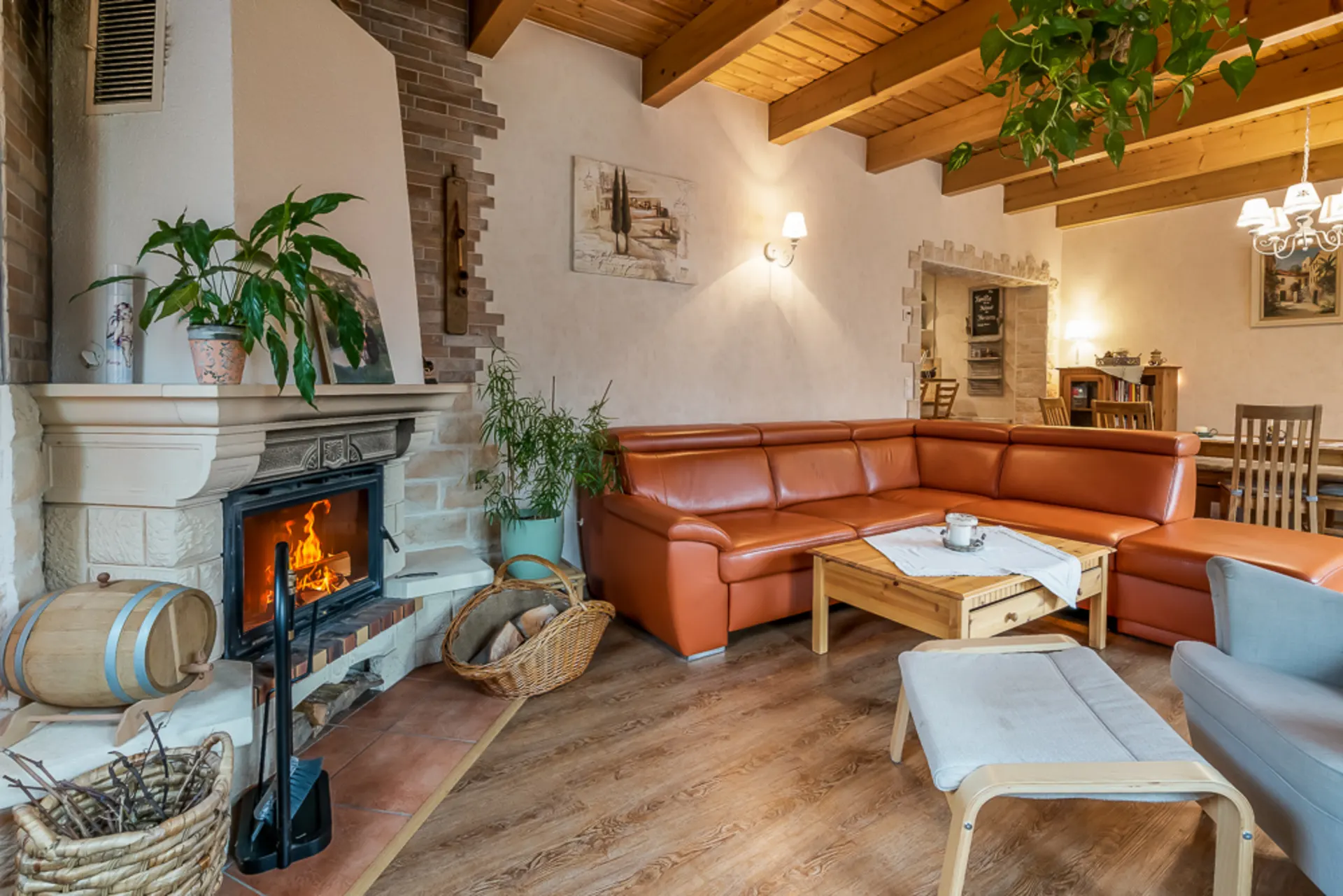 Gemütliches Wohnzimmer mit Kamin, orangefarbener Eckcouch und Holzbalkendecke.