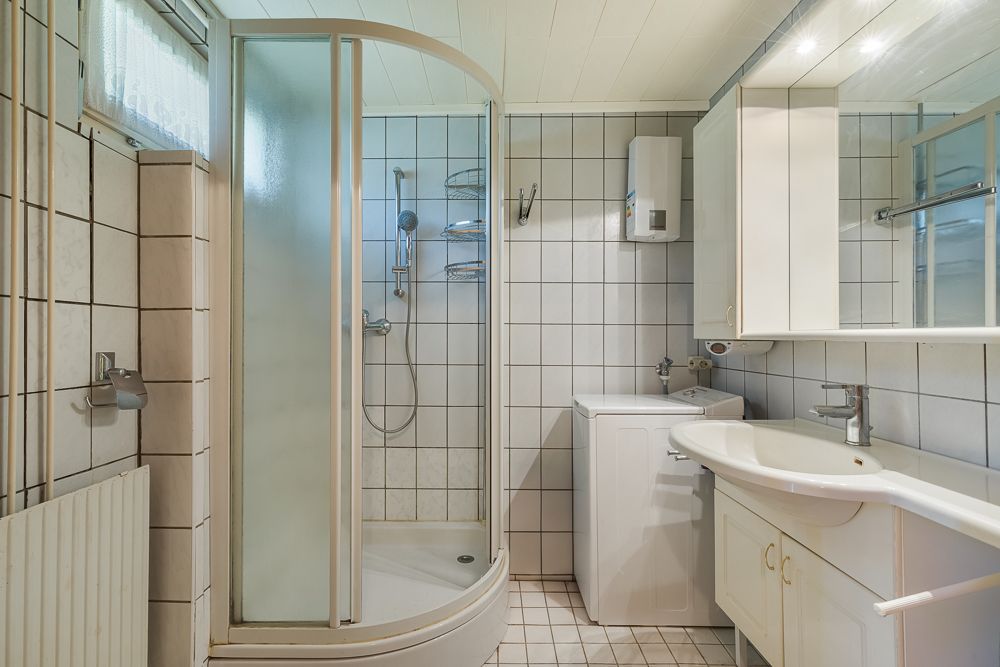 Helles Badezimmer mit Dusche, Waschbecken, Spiegelschrank und Waschmaschine.