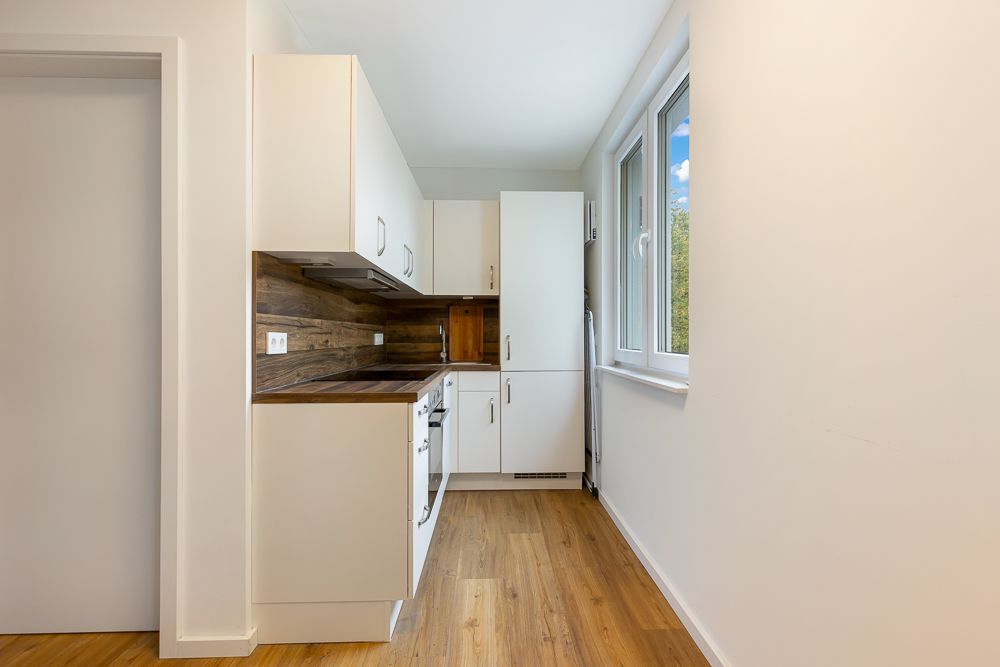 Helle, schmale Einbauküche mit Holzfußboden und weißen Schränken, Fenster rechts.