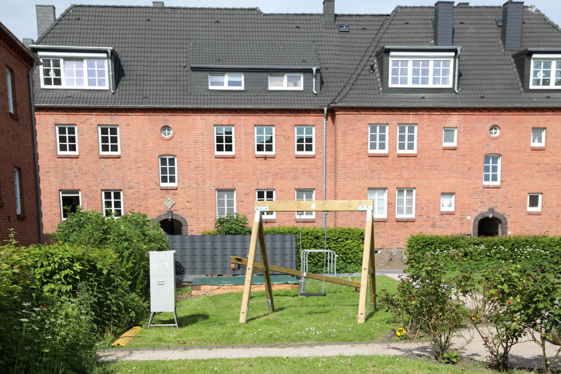 Grüner Hof mit Kinderschaukel, Rasen und roten Backsteinhäusern im Hintergrund.