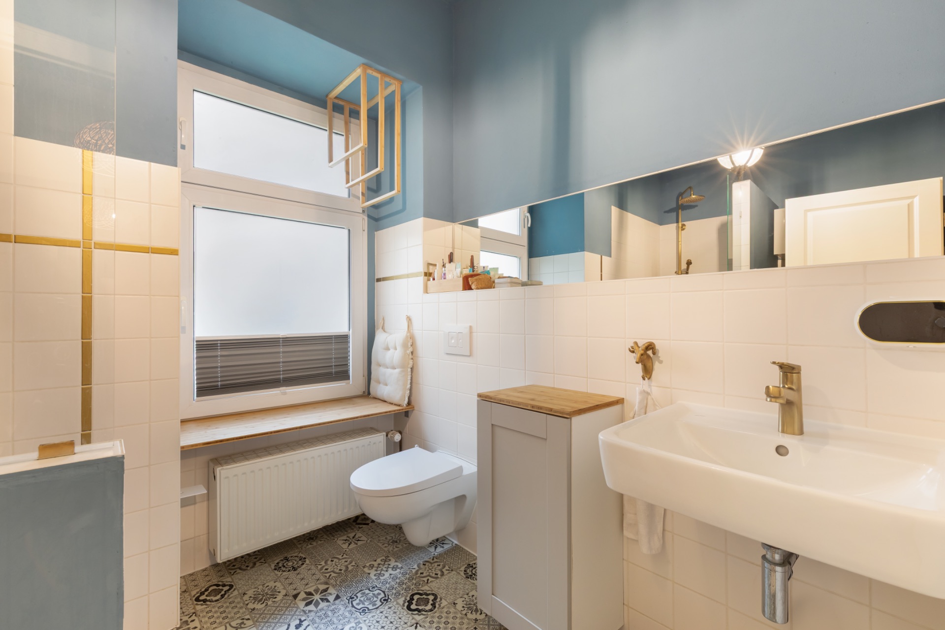 Helles Badezimmer mit Wandtoilette, Waschbecken, Fensterbank und großem Spiegel.