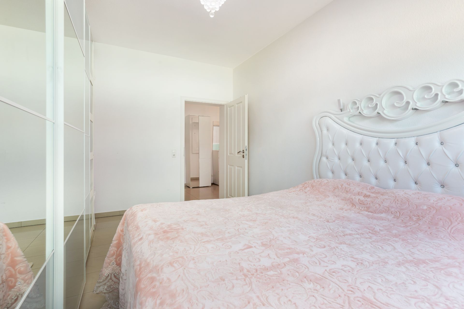 Helles Schlafzimmer mit großem Bett, gepolstertem Kopfteil und Spiegelschrank an der Wand.