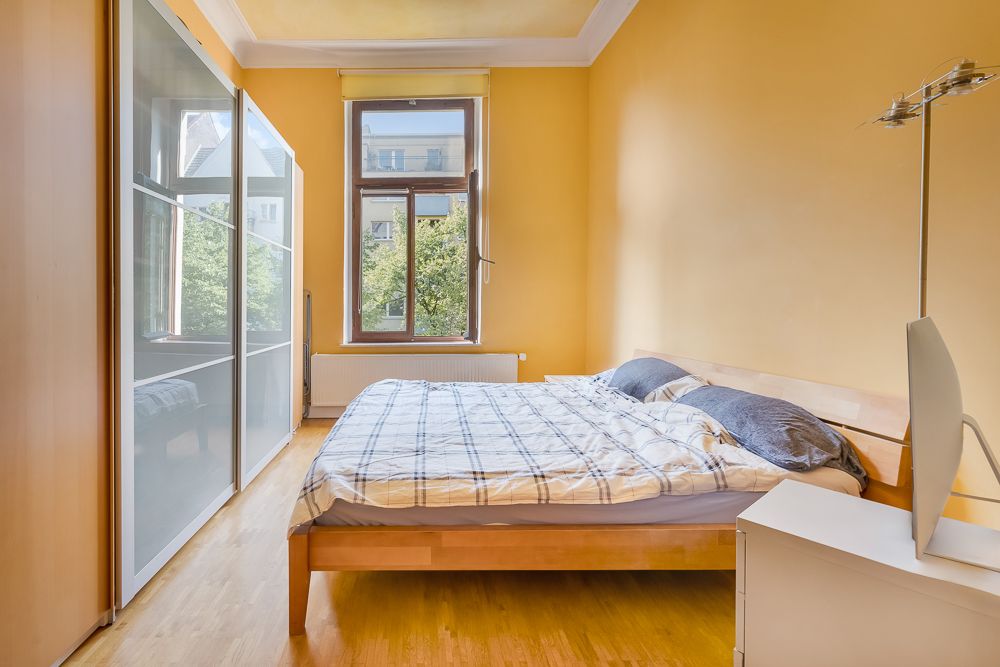 Schlafzimmer mit Doppelbett, großem Fenster, Kleiderschrank und gelben Wänden.