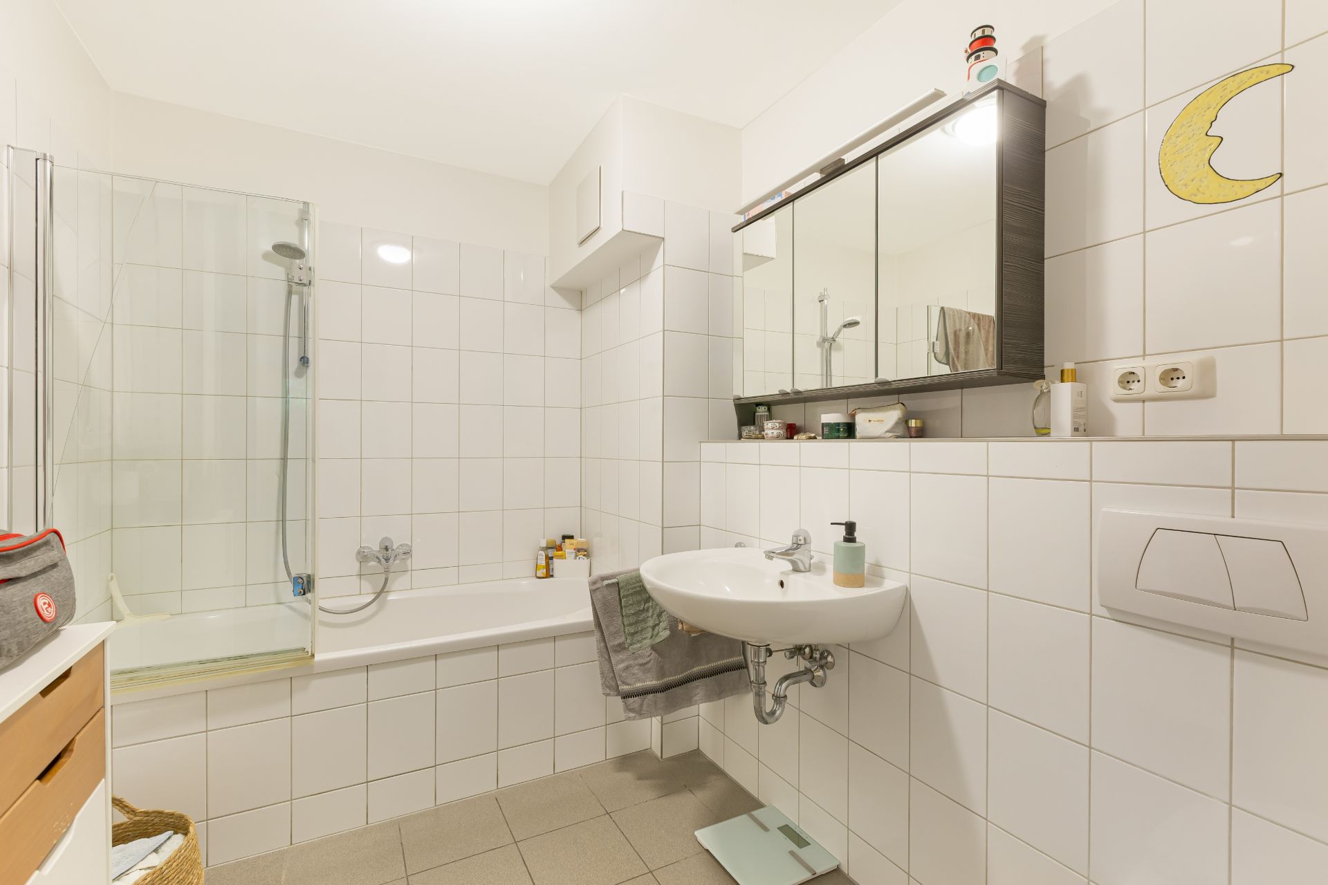 Helles Badezimmer mit Badewanne, Dusche, Waschbecken und Spiegelschrank, weiße Fliesen an den Wänden.