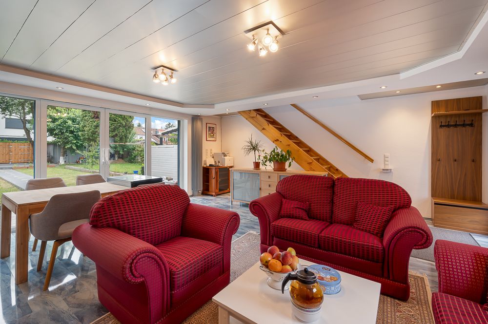 Wohnzimmer mit roten Sofas, Couchtisch, großem Fenster und Holztreppe.