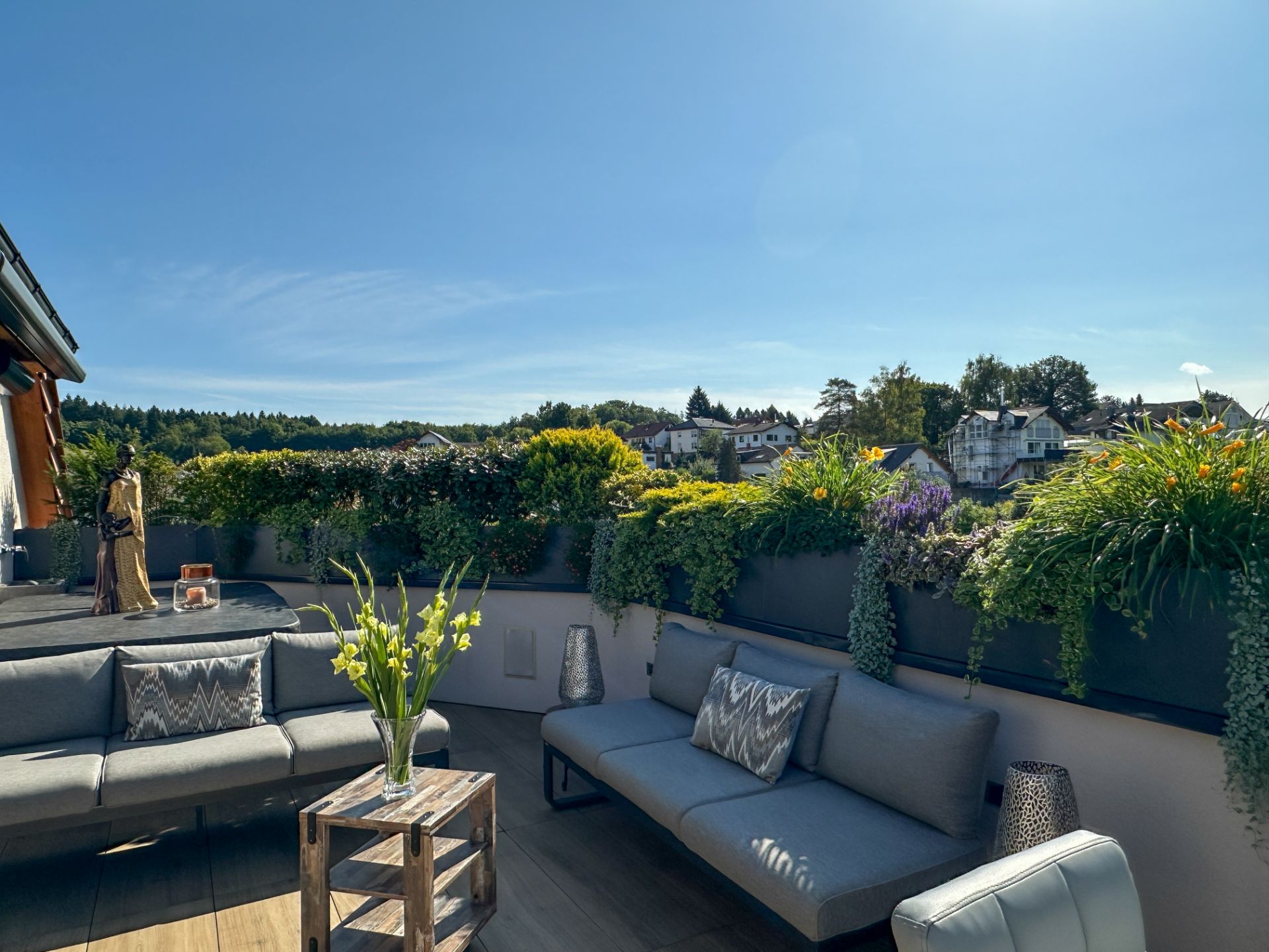 Moderne Dachterrasse mit grauen Sofas, Pflanzen und Blick auf umliegende Häuser.