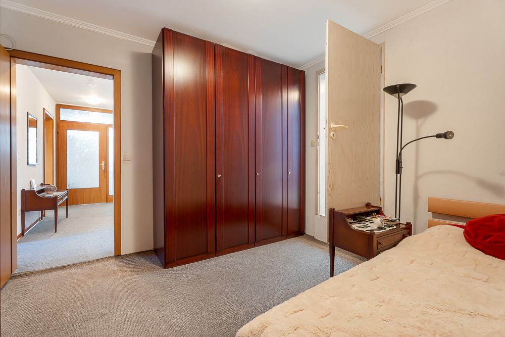 Schlafzimmer mit großem Holzkleiderschrank, Bett, Nachttisch und Stehlampe.