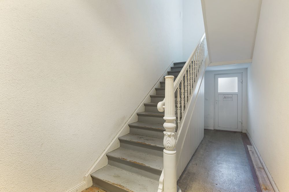 Helle Treppenhaus mit grauer Treppe und weißem Geländer, Tür am Ende des Flurs.