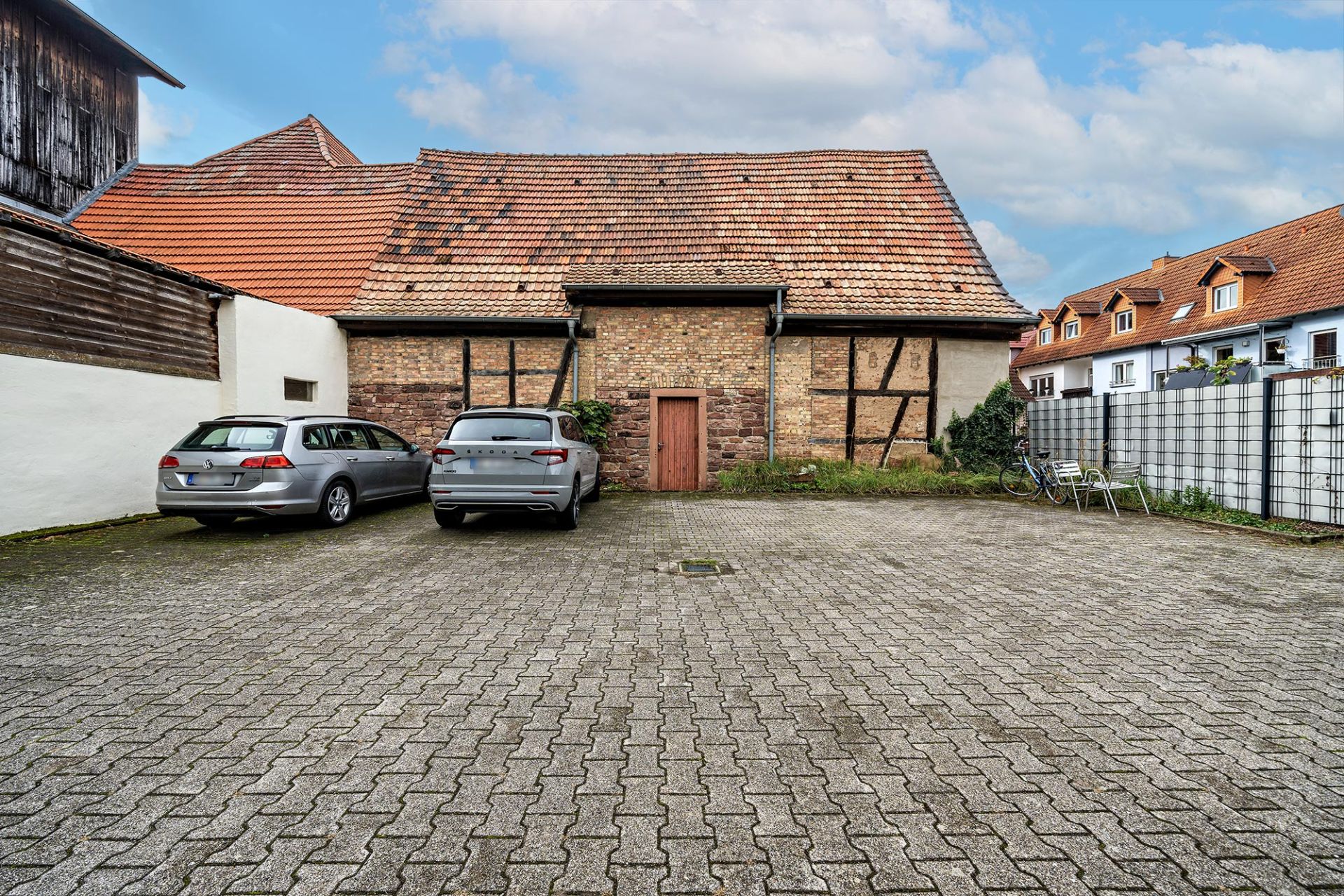 Gepflasterter Hof mit zwei Autos, altem Gebäude und einem Tisch mit Stühlen am Rand.