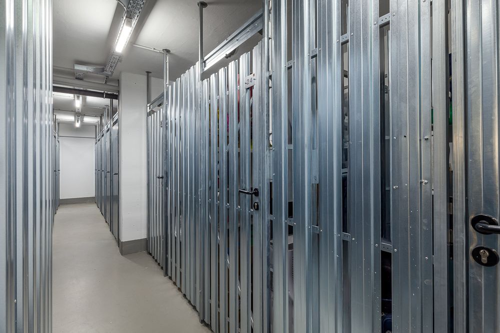Gang mit mehreren Metallverschlägen in einem Kellerbereich, helle Beleuchtung.