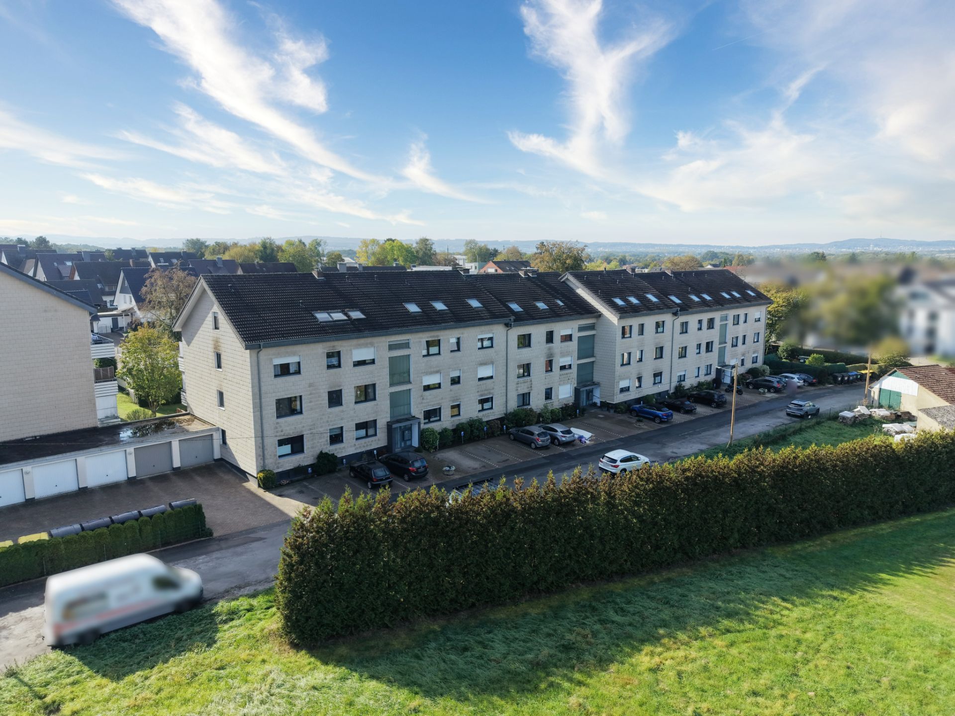 Langes, dreistöckiges Wohnhaus mit mehreren Autos auf dem Parkplatz davor.