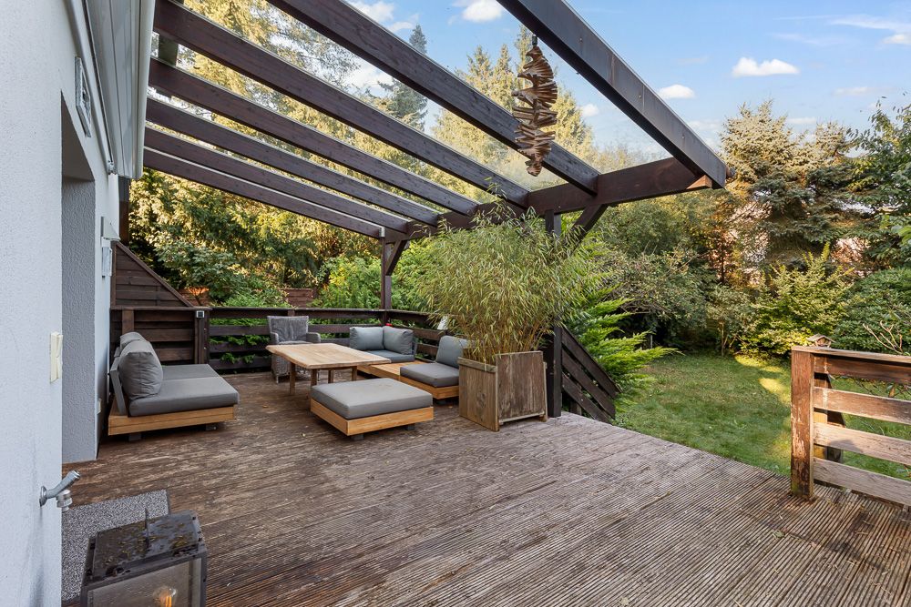 Überdachte Holzterrasse mit Sitzmöbeln und Pflanzen, Blick in einen grünen Garten.