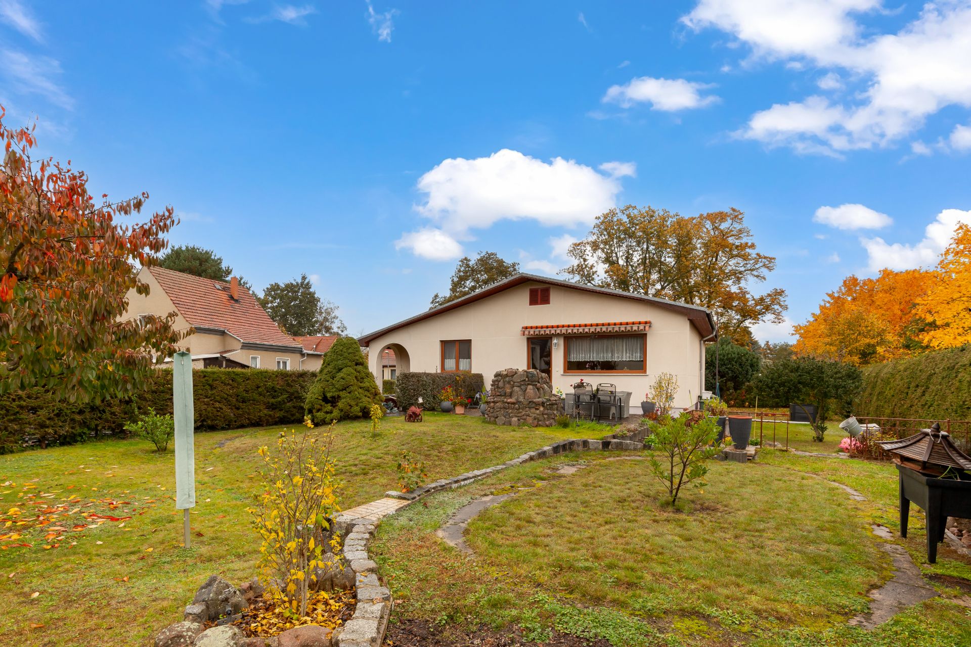 Einfamilienhaus mit Garten, Rasenfläche, Bäumen und buntem Herbstlaub im Hintergrund.