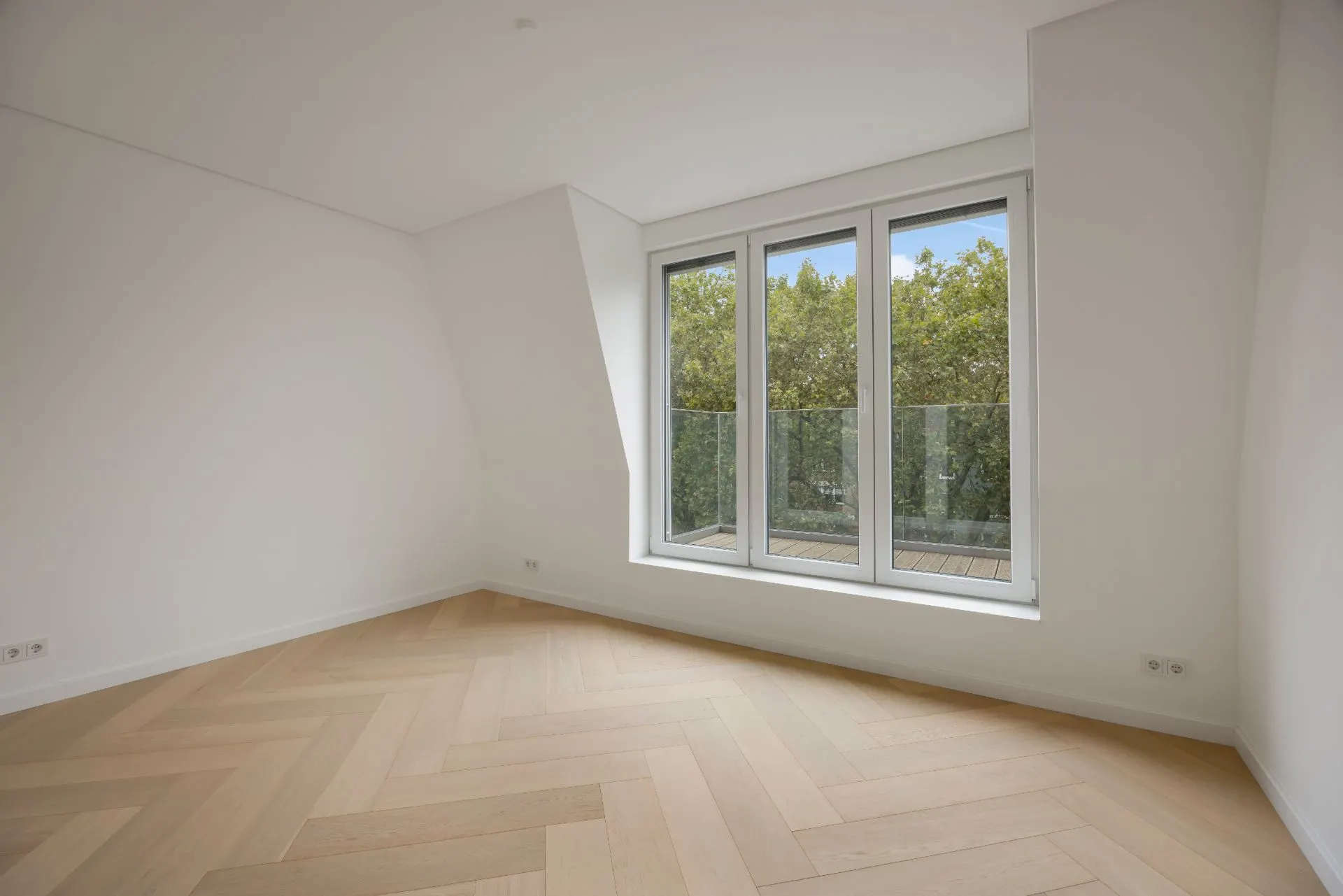 Leerer Raum mit hellem Holzfußboden und großen Fenstern zu einem Balkon mit Blick ins Grüne.