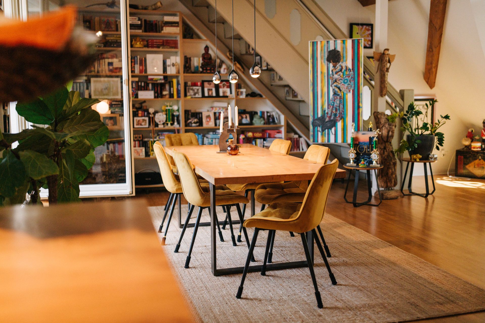 Esszimmer mit Holztisch, gelben Stühlen und Bücherregal unter einer Treppe.