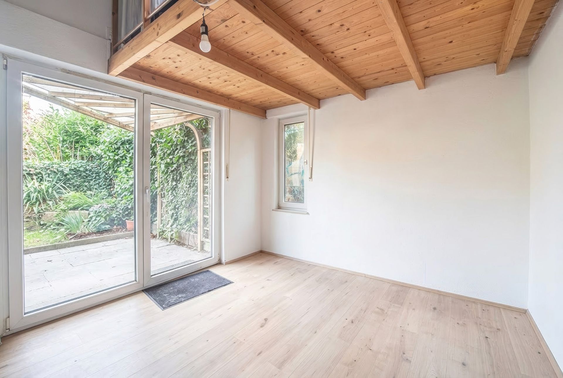 Heller Raum mit Holzdecke, großem Fenster und Glastür zum Garten.