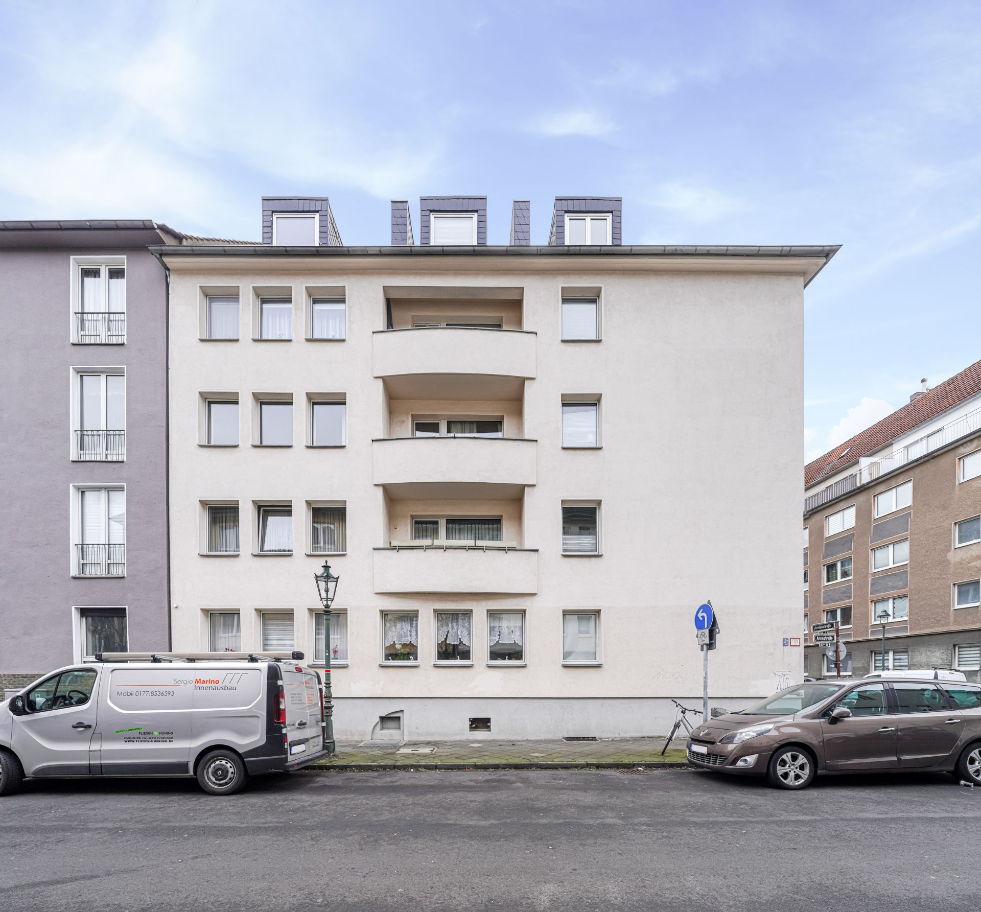 Wohnhaus mit zwei mittigen Balkonen, geparkte Autos davor an der Straße.
