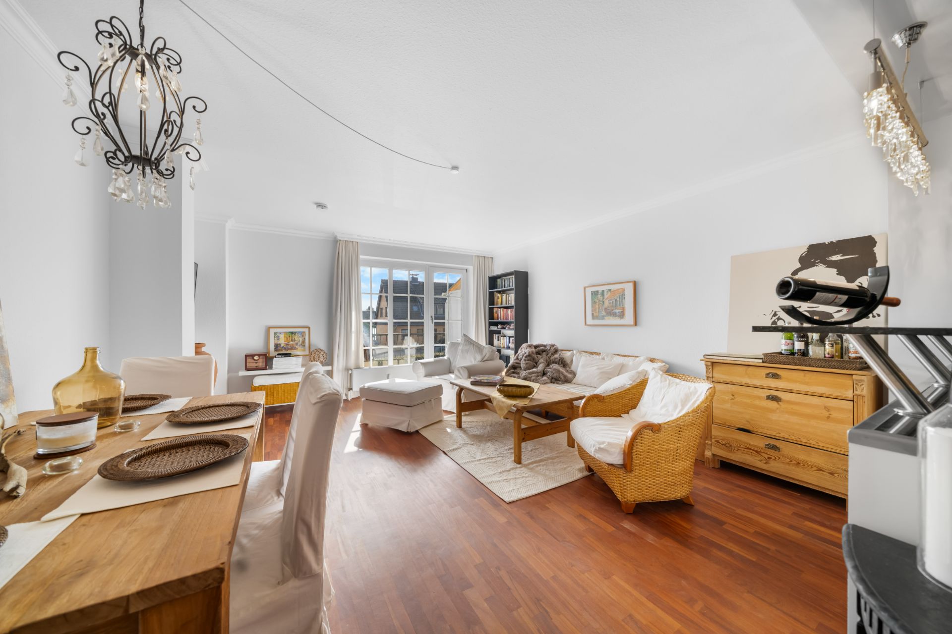 Helles Wohnzimmer mit Essbereich, Holzboden, Sofa, Sesseln und großem Fenster.
