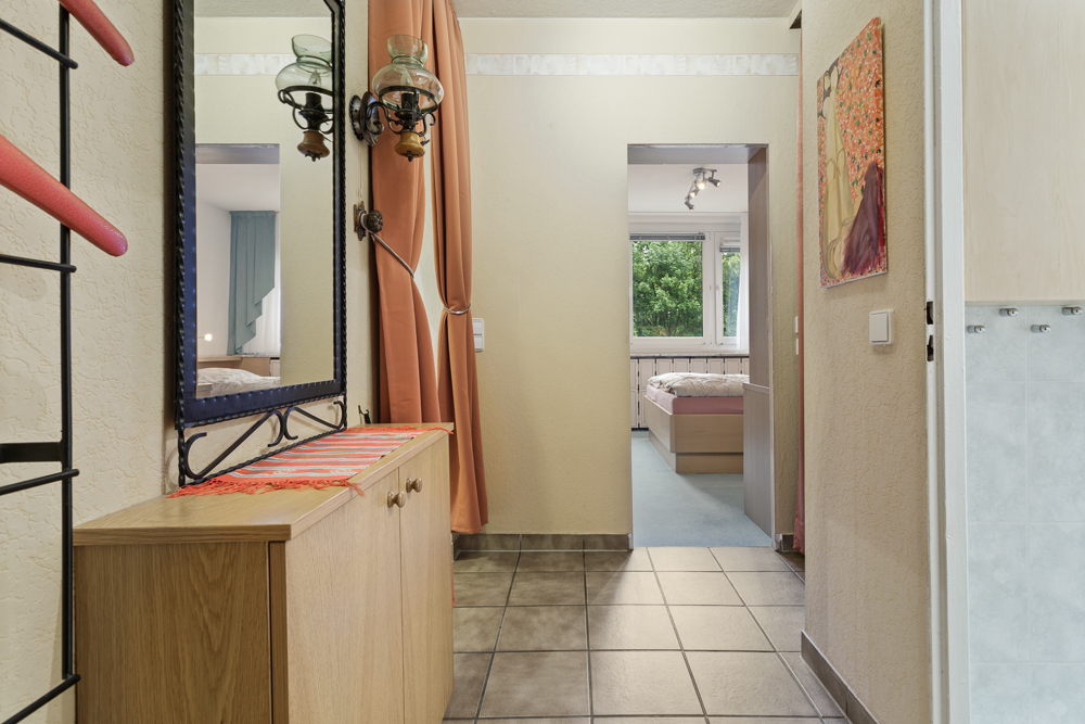 Flur mit Spiegel, Kommode und Blick in ein Schlafzimmer mit großem Fenster.