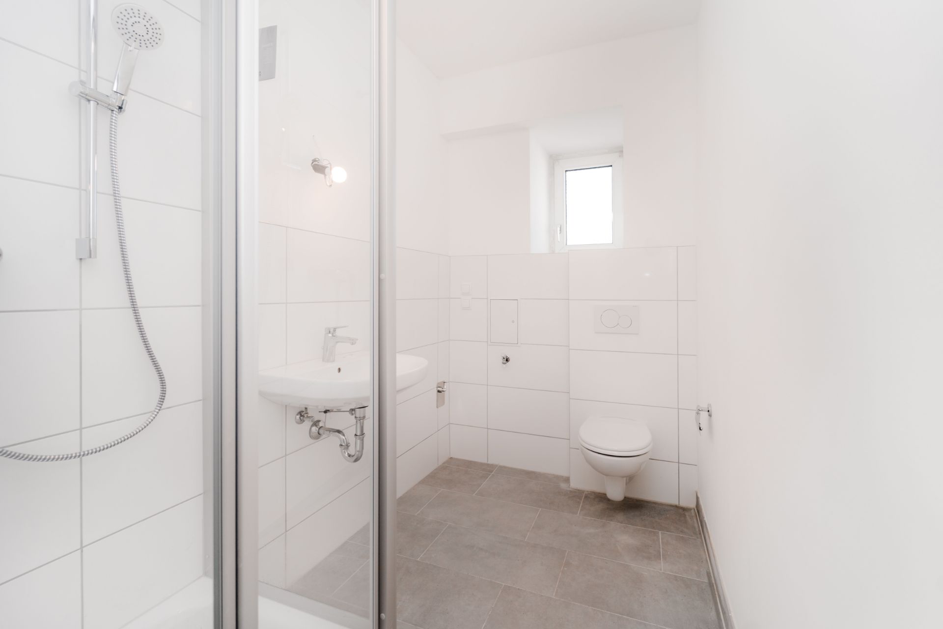 Helles Badezimmer mit Dusche, Waschbecken, WC und kleinem Fenster.