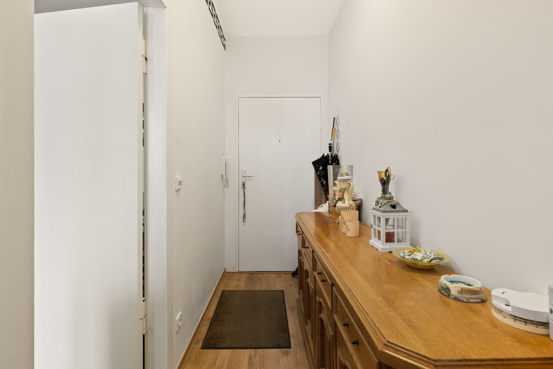 Flur mit Holzboden, weißer Tür, Holzkommode und Dekorationen.