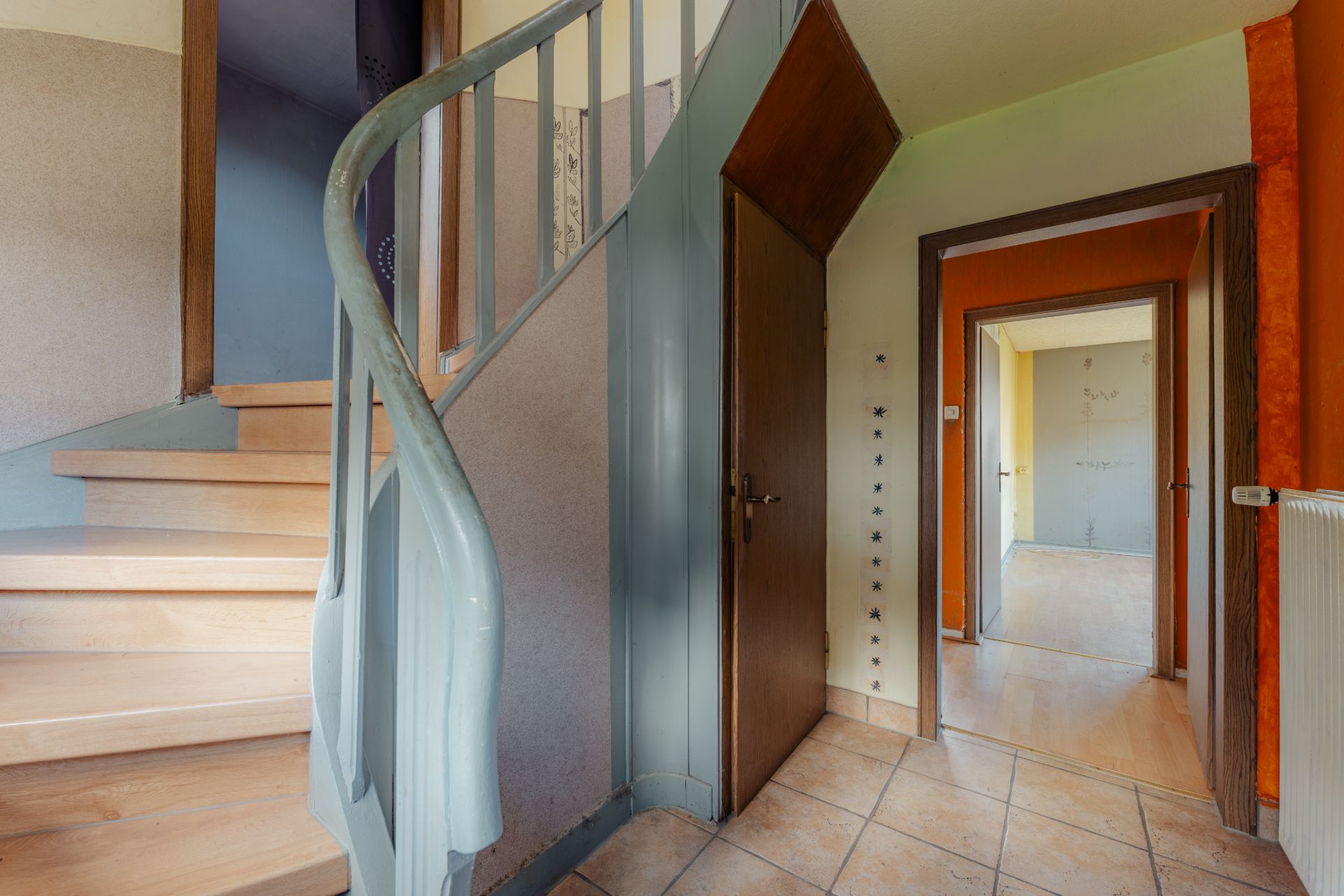 Flur mit Treppe, Fliesenboden, Holzstufen und mehreren Türen zu angrenzenden Räumen.