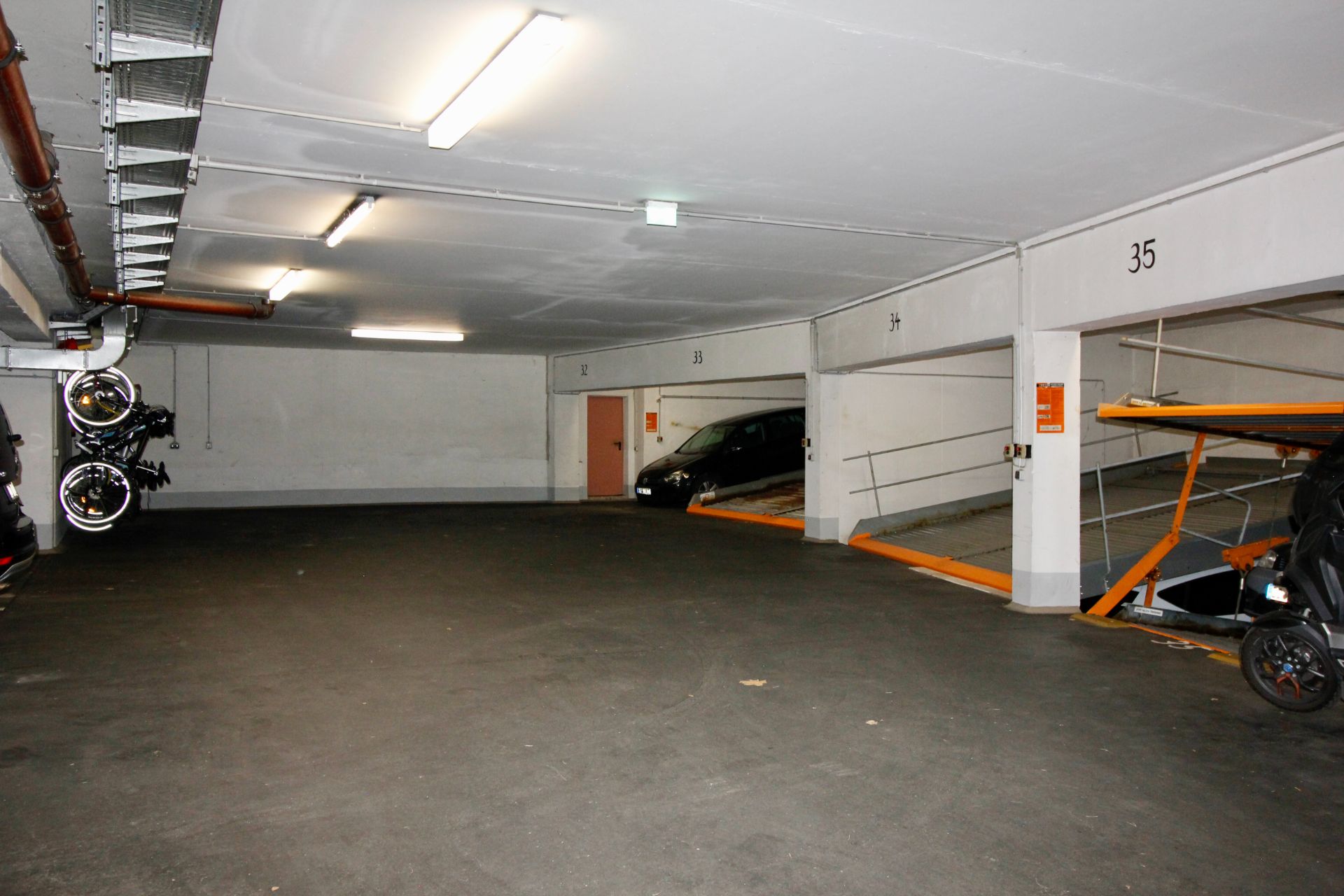 Tiefgarage mit markierten Parkplätzen, Fahrrädern an der Wand und Autos auf Parkebenen.