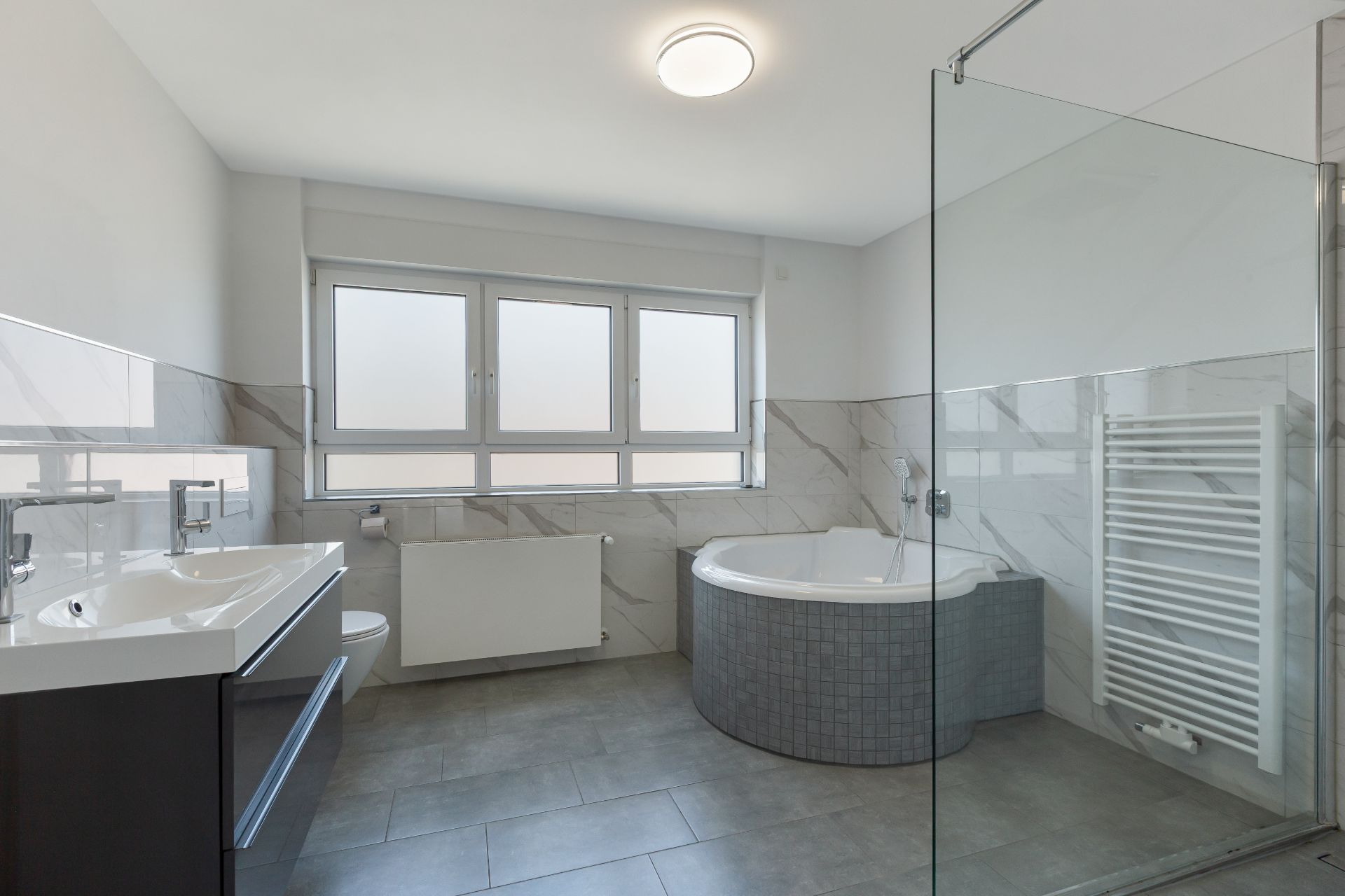 Modernes Badezimmer mit Eckbadewanne, Doppelwaschbecken und großem Fenster.