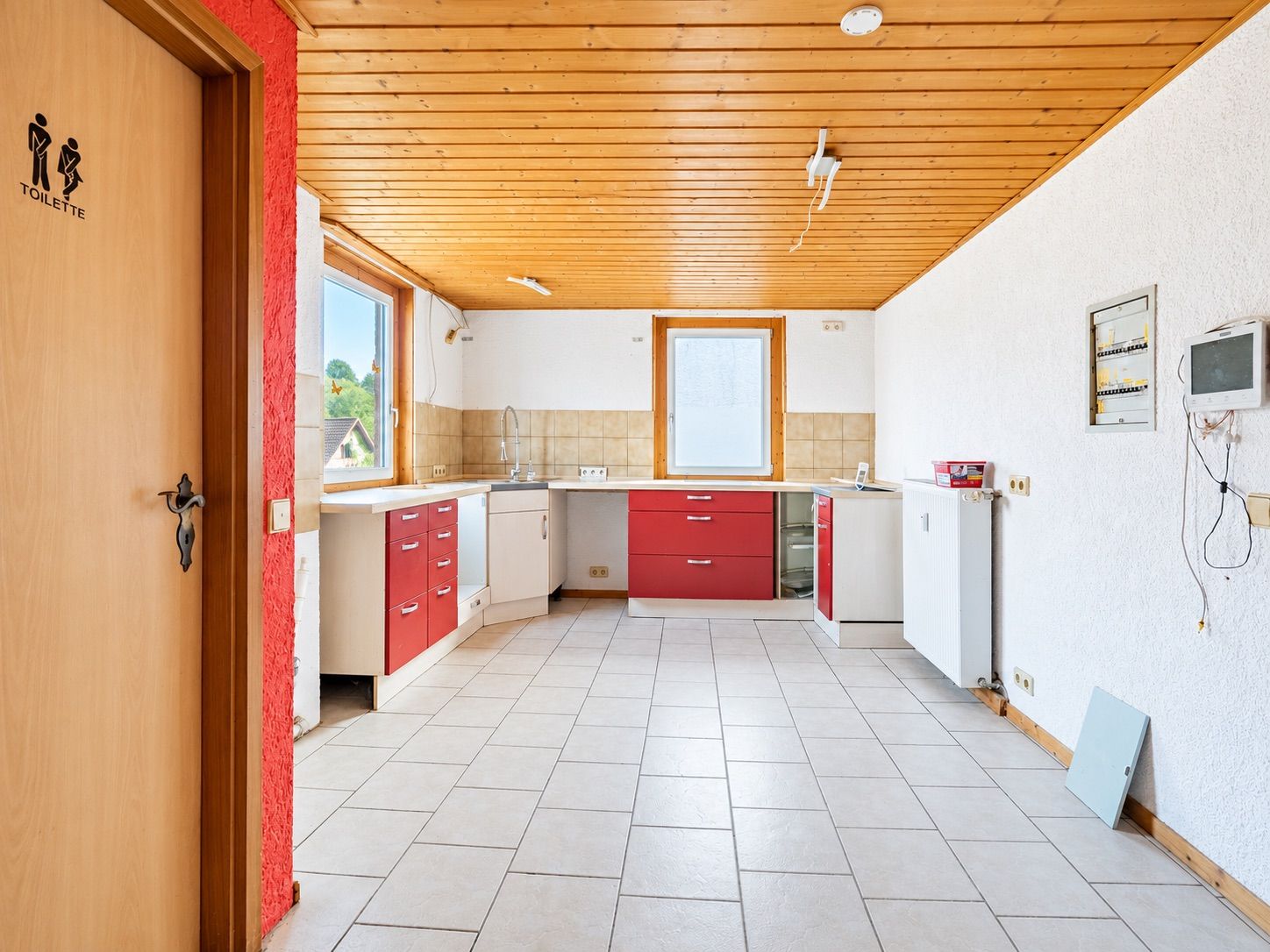 Leere helle Küche mit roten Unterschränken, Holzbalkendecke und Fliesenboden.