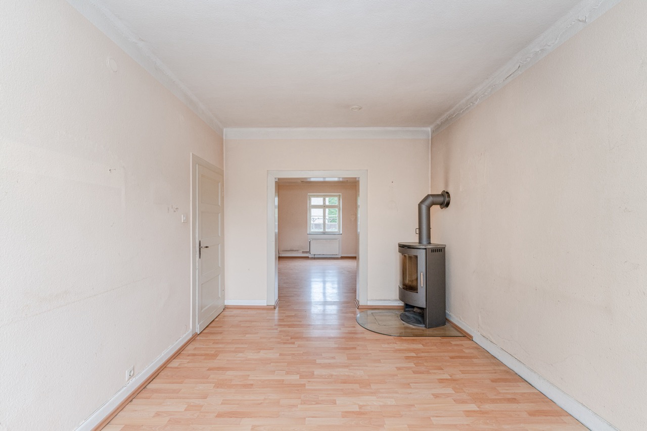 Heller Raum mit Laminatboden, weißen Wänden und einem Kaminofen an der rechten Wand.