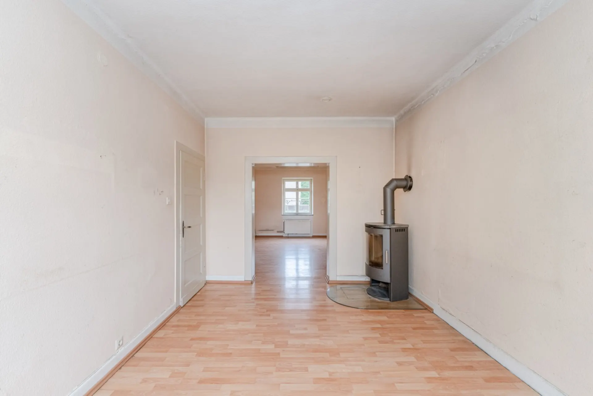 Heller Raum mit Laminatboden, weißen Wänden und einem Kaminofen an der rechten Wand.