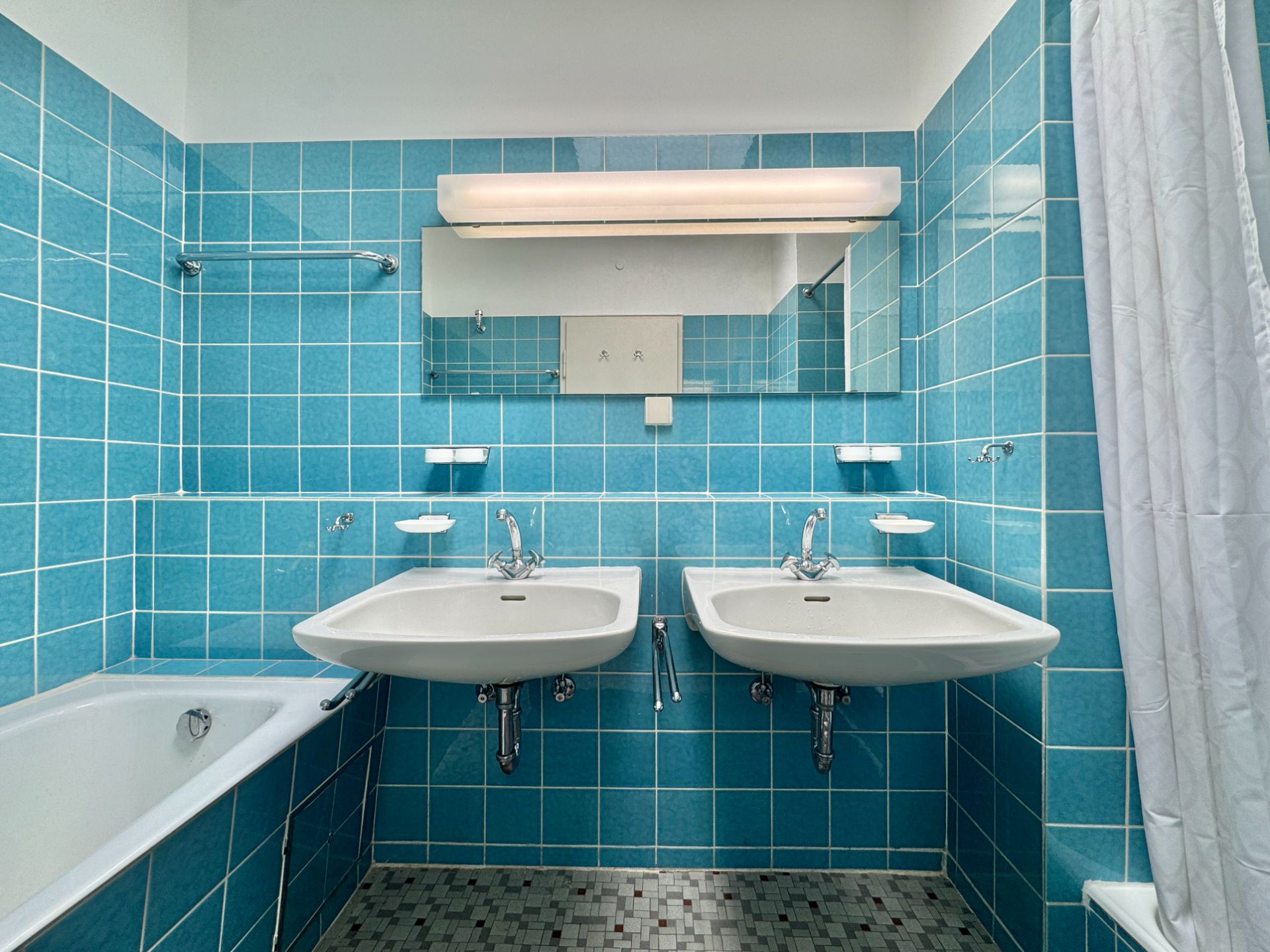 Badezimmer mit zwei Waschbecken, Badewanne und blauen Fliesen.