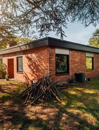 Backsteinbungalow mit flachem Dach und Garten, Holz und Leiter an der Hauswand.