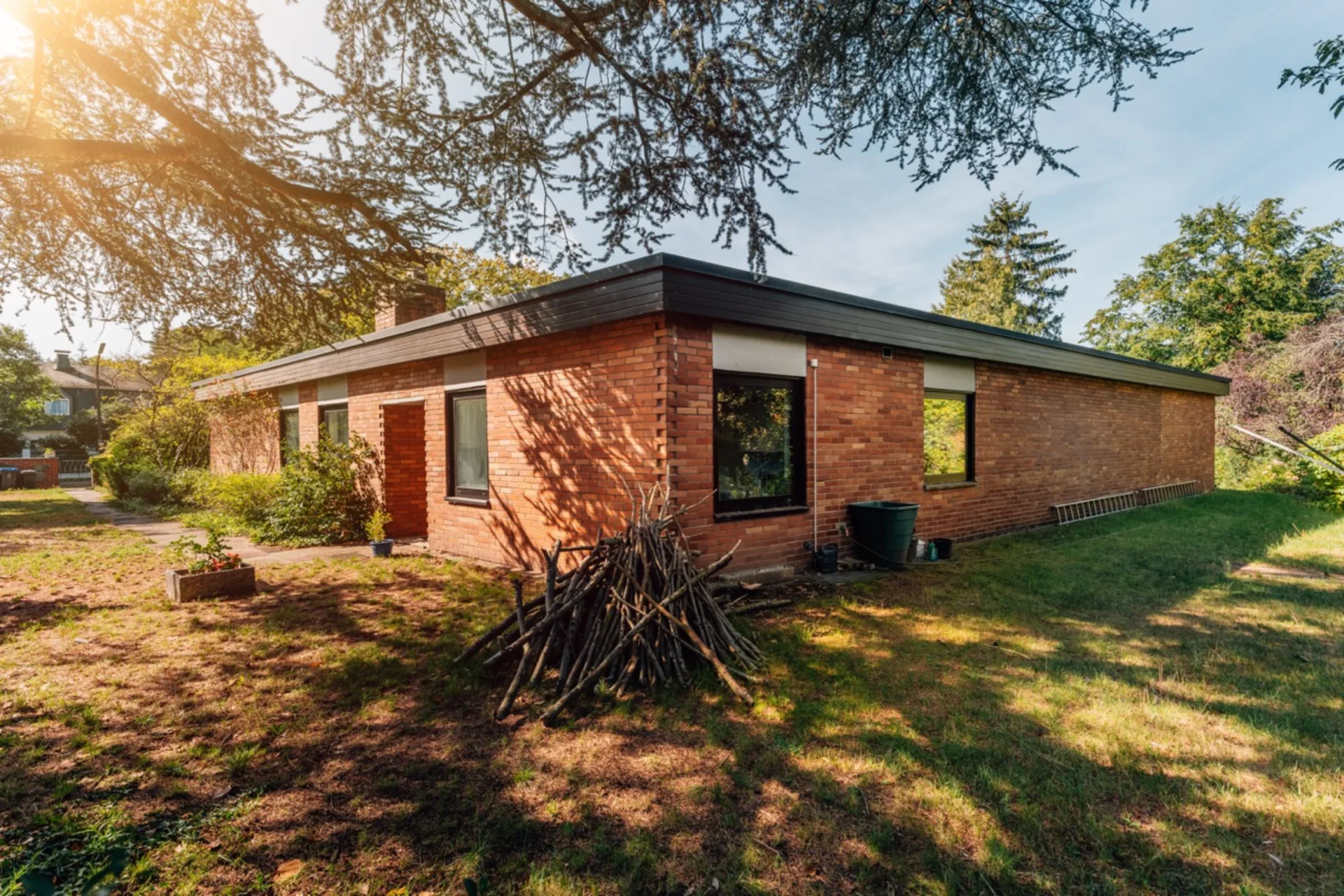 Backsteinbungalow mit flachem Dach und Garten, Holz und Leiter an der Hauswand.