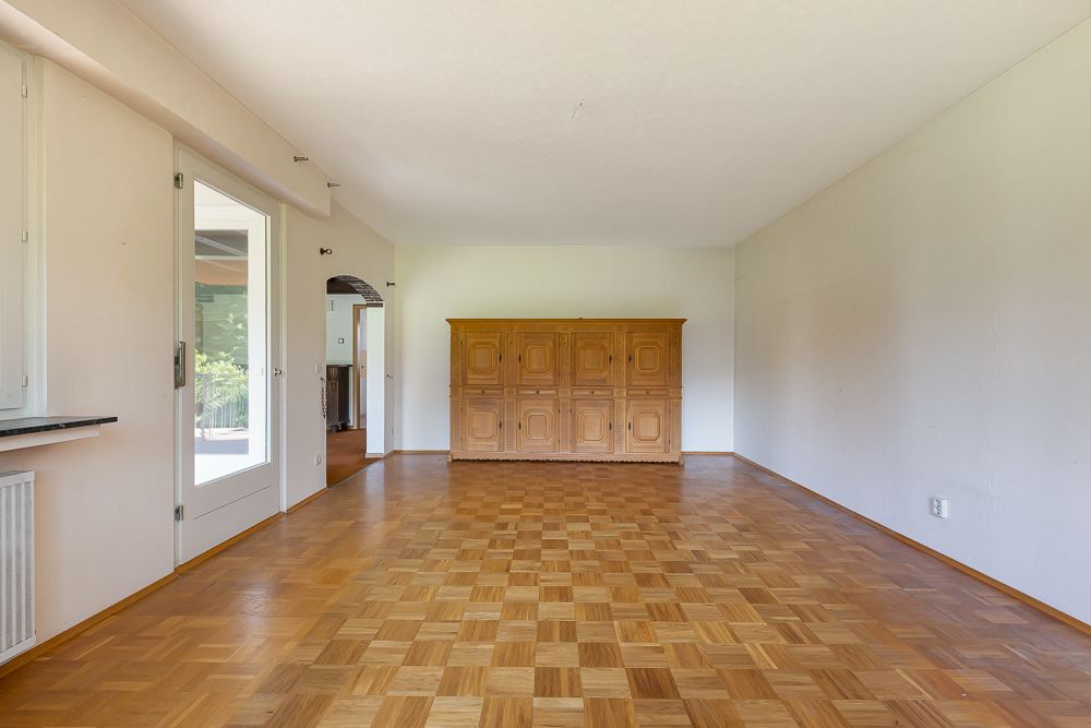 Leeres Wohnzimmer mit Parkettboden und großem Holzschrank an der Rückwand.