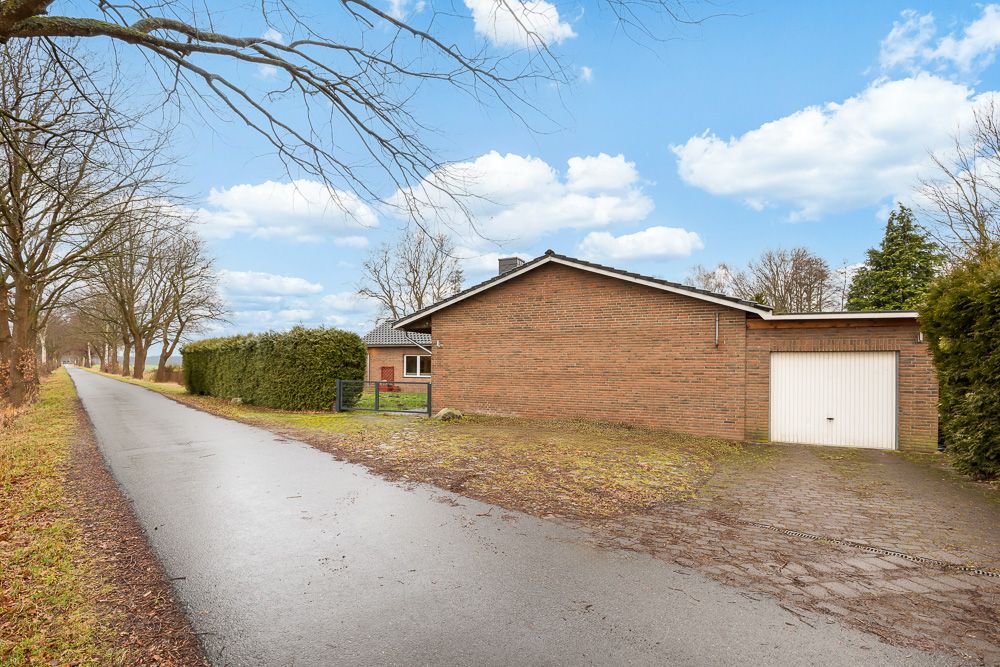 Backsteinwohnhaus mit angebauter Garage an ruhiger Straße, umgeben von Bäumen und Hecken.