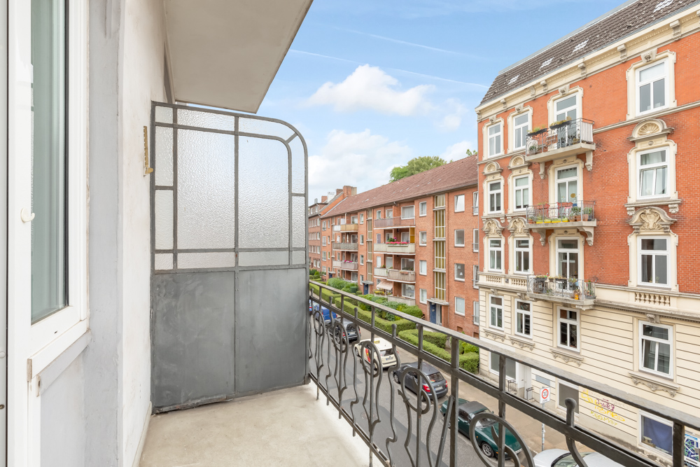 Balkon mit Metallgeländer und Sichtschutz, Blick auf Wohnstraße und rote Backsteingebäude.