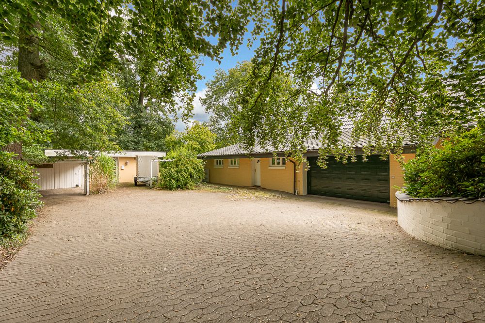 Gepflasterter Hof mit gelbem Wohnhaus, großer Garage und umgebenden Bäumen.