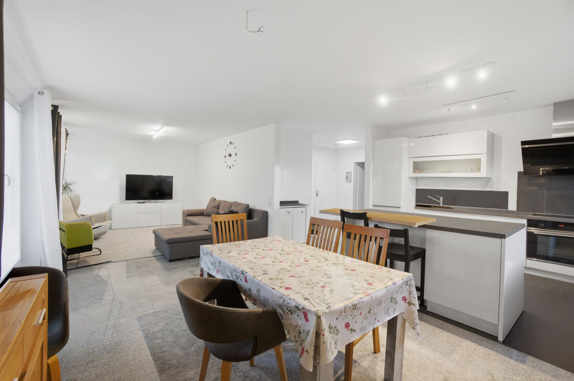 Helles Wohnzimmer mit Sofa, TV, Essbereich und offener Küche mit Kochinsel.