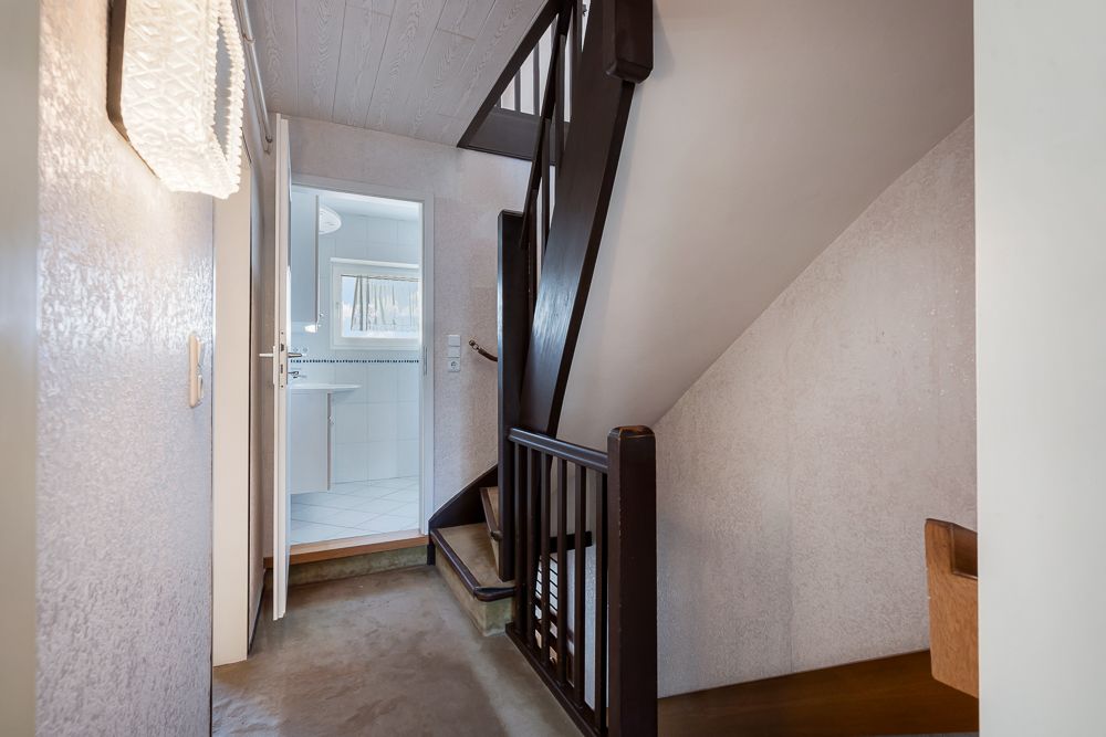 Flur mit Treppe und offenem Zugang zum Badezimmer mit Fenster.