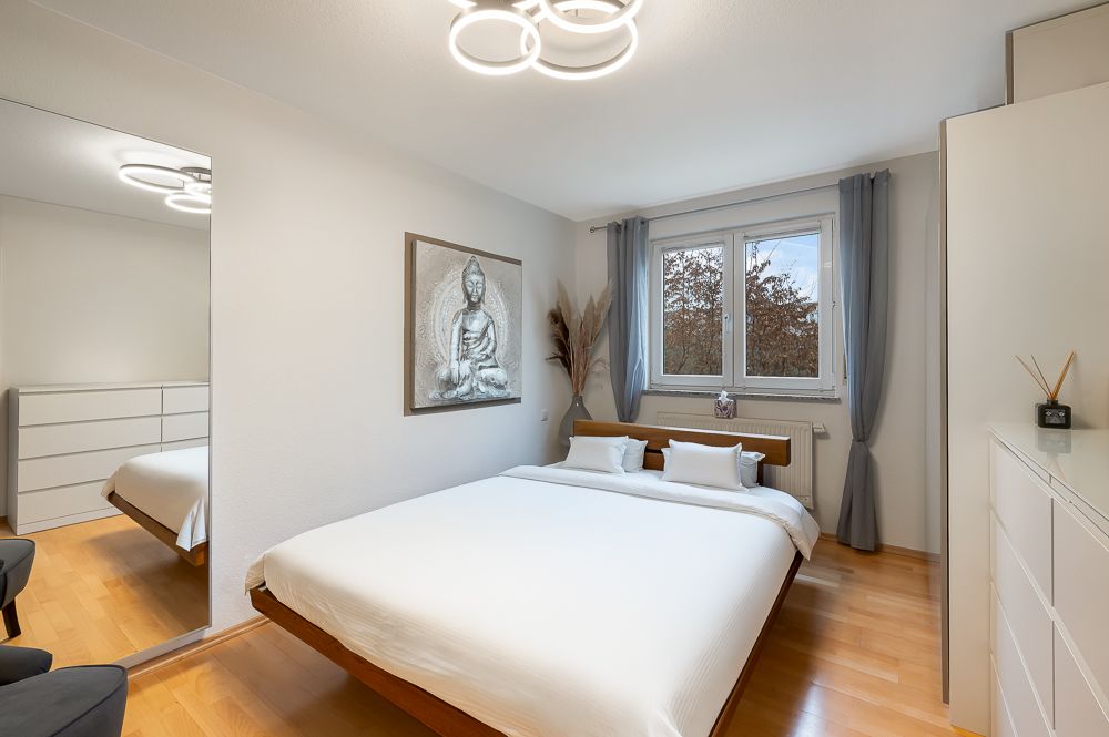 Helles Schlafzimmer mit Doppelbett, großem Spiegel, Fenster und Buddha-Bild an der Wand.